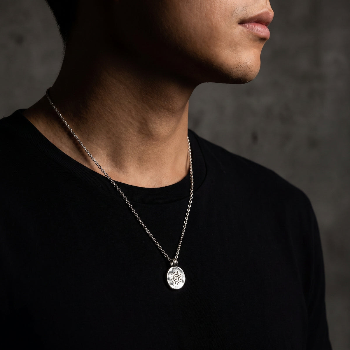 Side view of a man wearing the silver sunburst disc pendant on a chain over a black T-shirt.