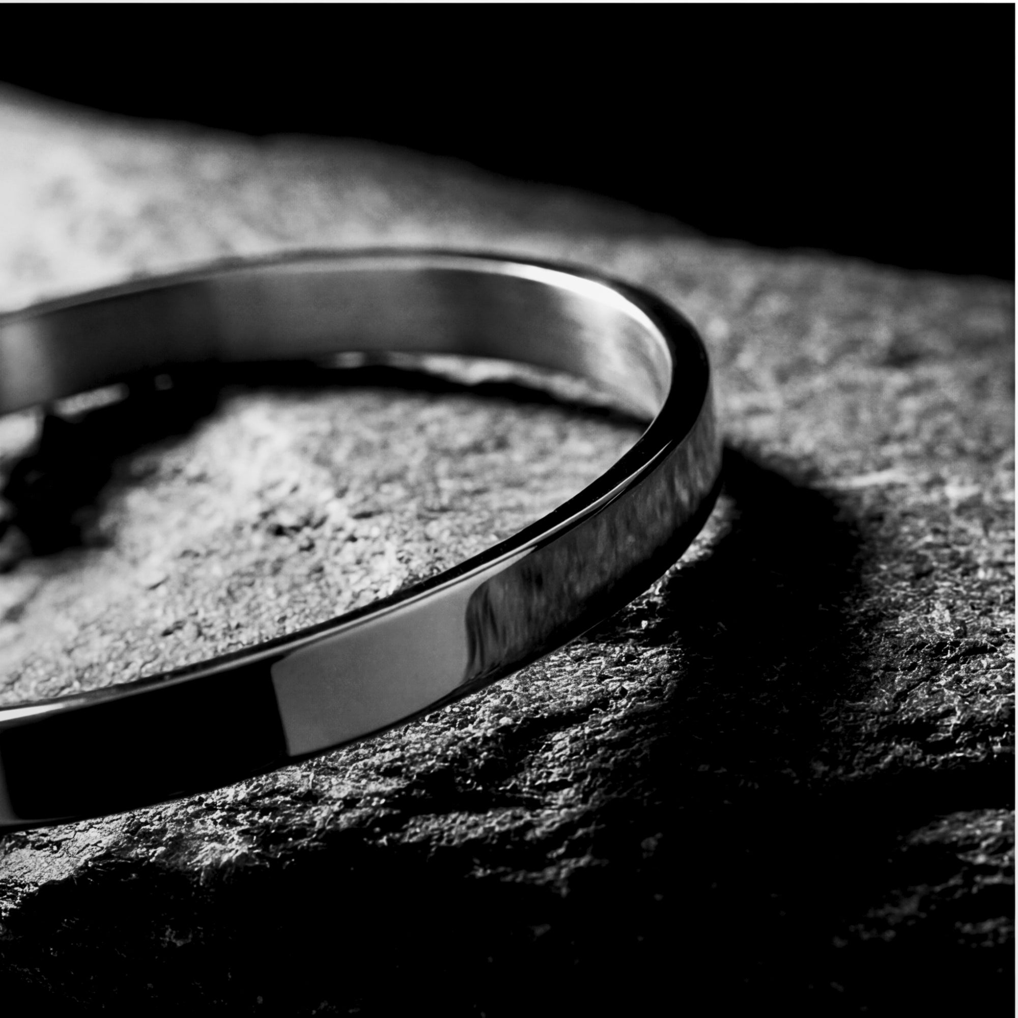 Close-up of a polished silver stainless steel cuff bracelet showing its smooth 5mm width on a rock.