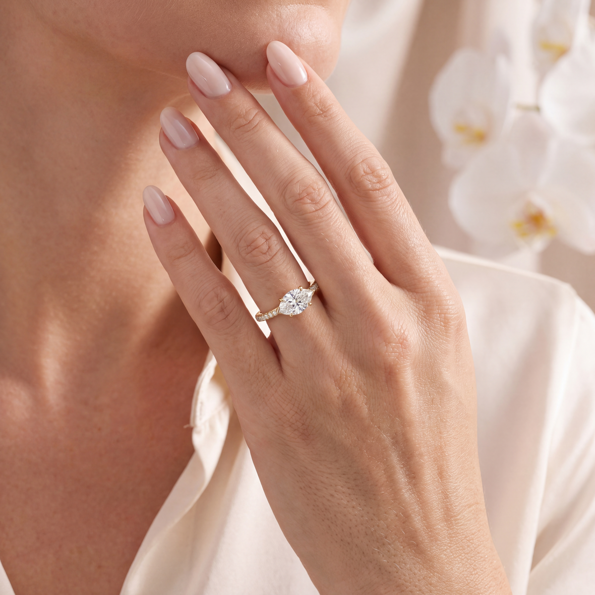 Yellow gold east-west marquise moissanite engagement ring with a pavé band worn on a model's hand.