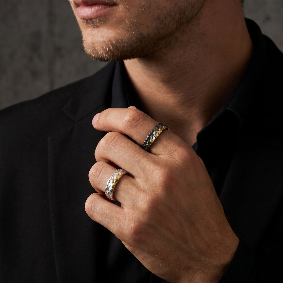 Close-up of a man wearing dark-toned and bright silver open-band rings with gold mountain reliefs on two fingers.
