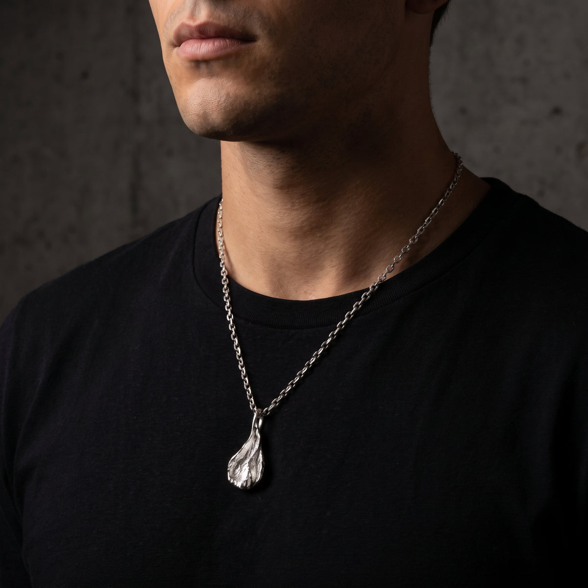 Close-up front view of a model wearing the silver petal pendant necklace over a black shirt.