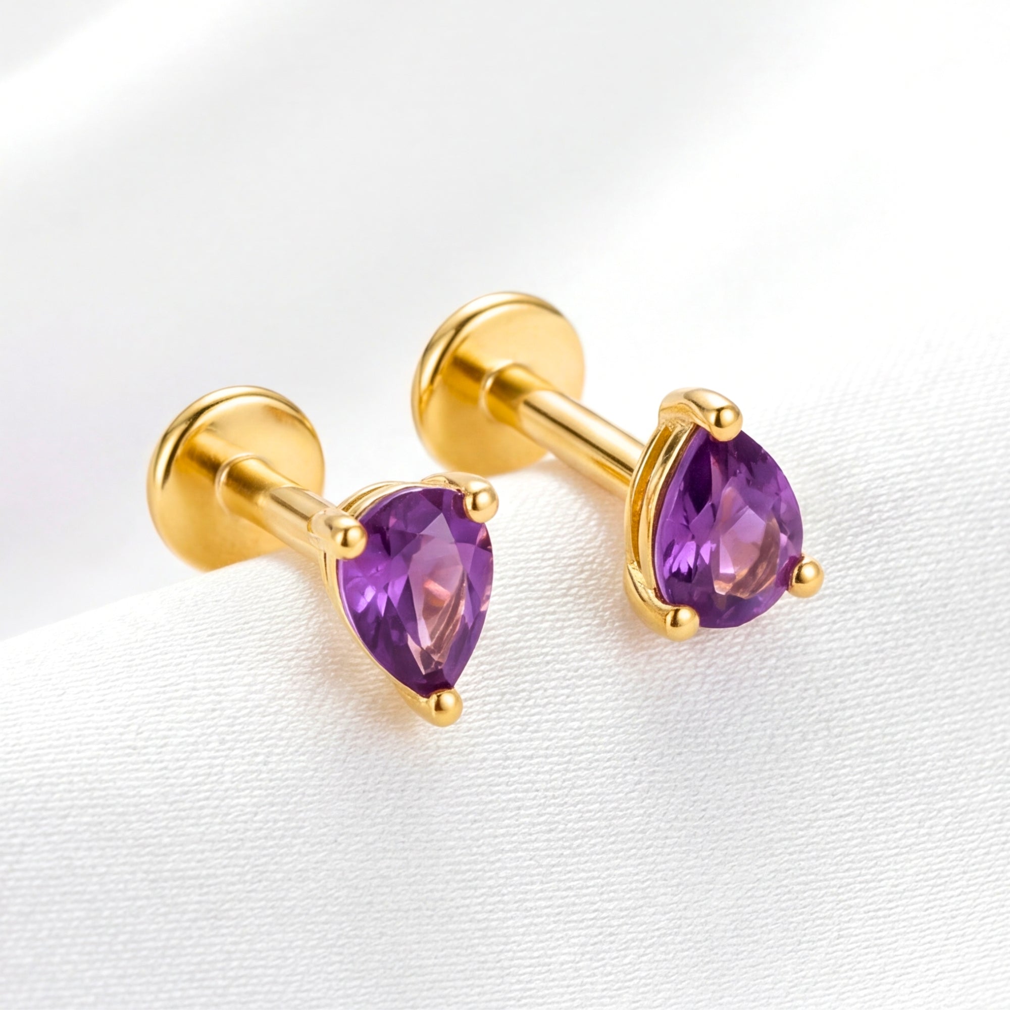 Teardrop purple simulated amethyst earrings in 18K gold vermeil with flat-back labret design on white silk.