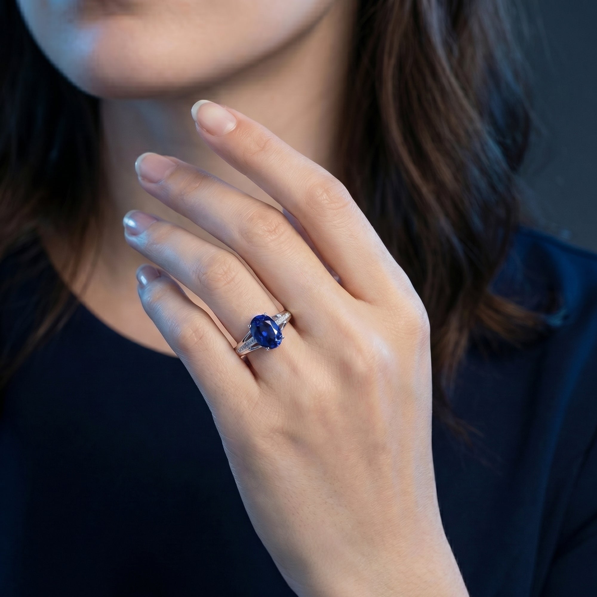 The 18K white gold oval tanzanite and diamond ring worn on a model's hand.