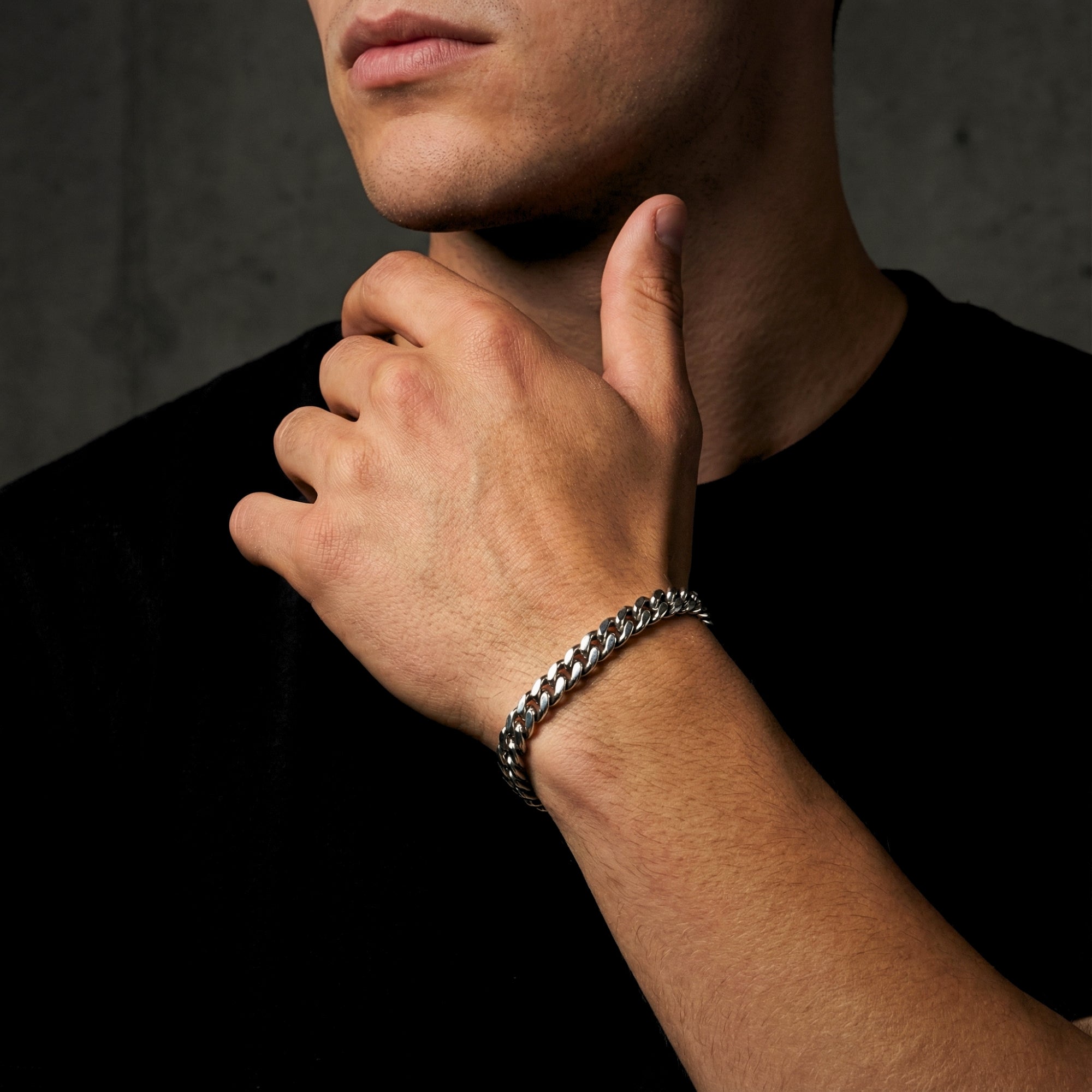 Men's silver stainless steel Cuban link bracelet worn on a wrist, paired with a black t-shirt.