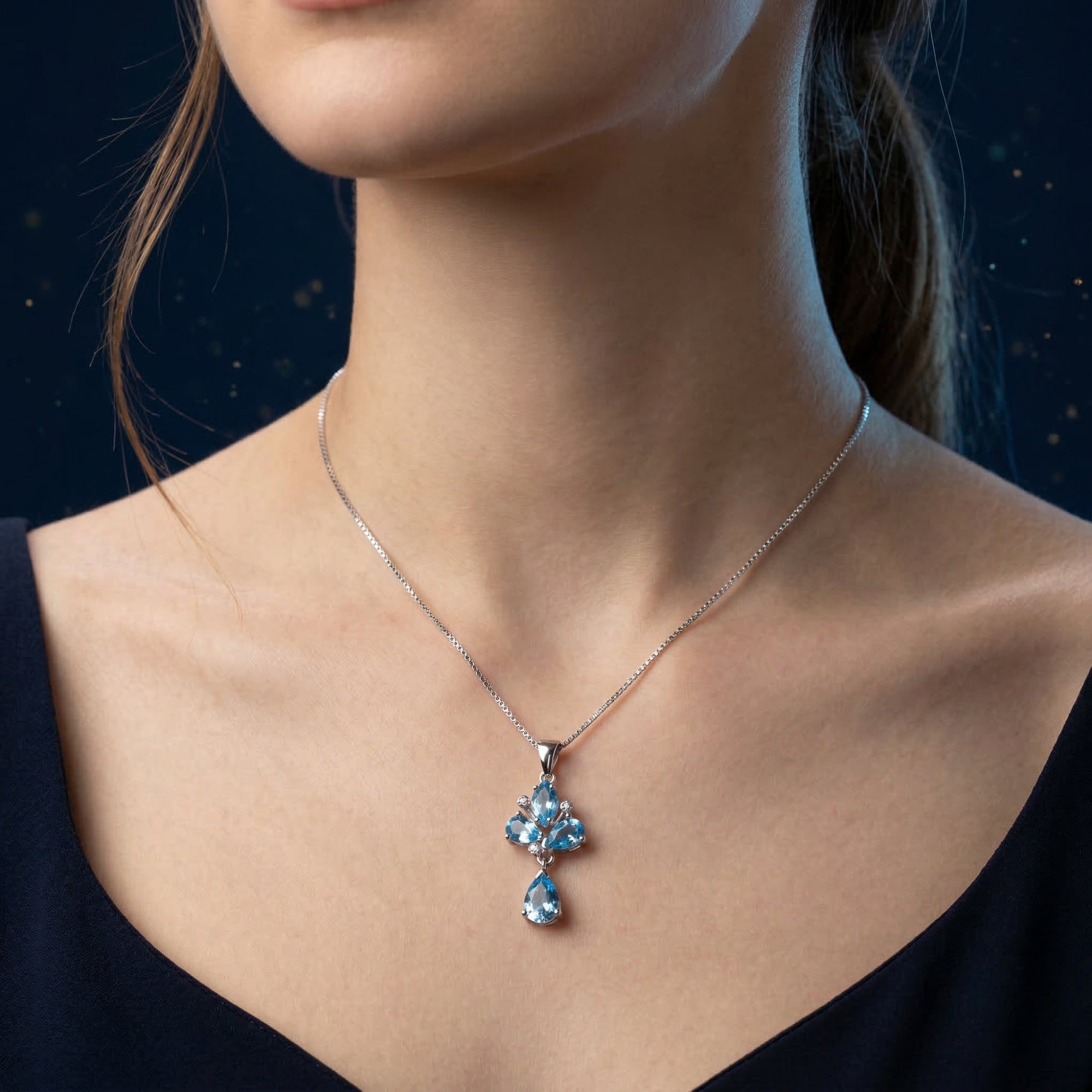 Woman wearing the Zephyrine silver necklace featuring pear and marquise cut natural Swiss blue topaz.