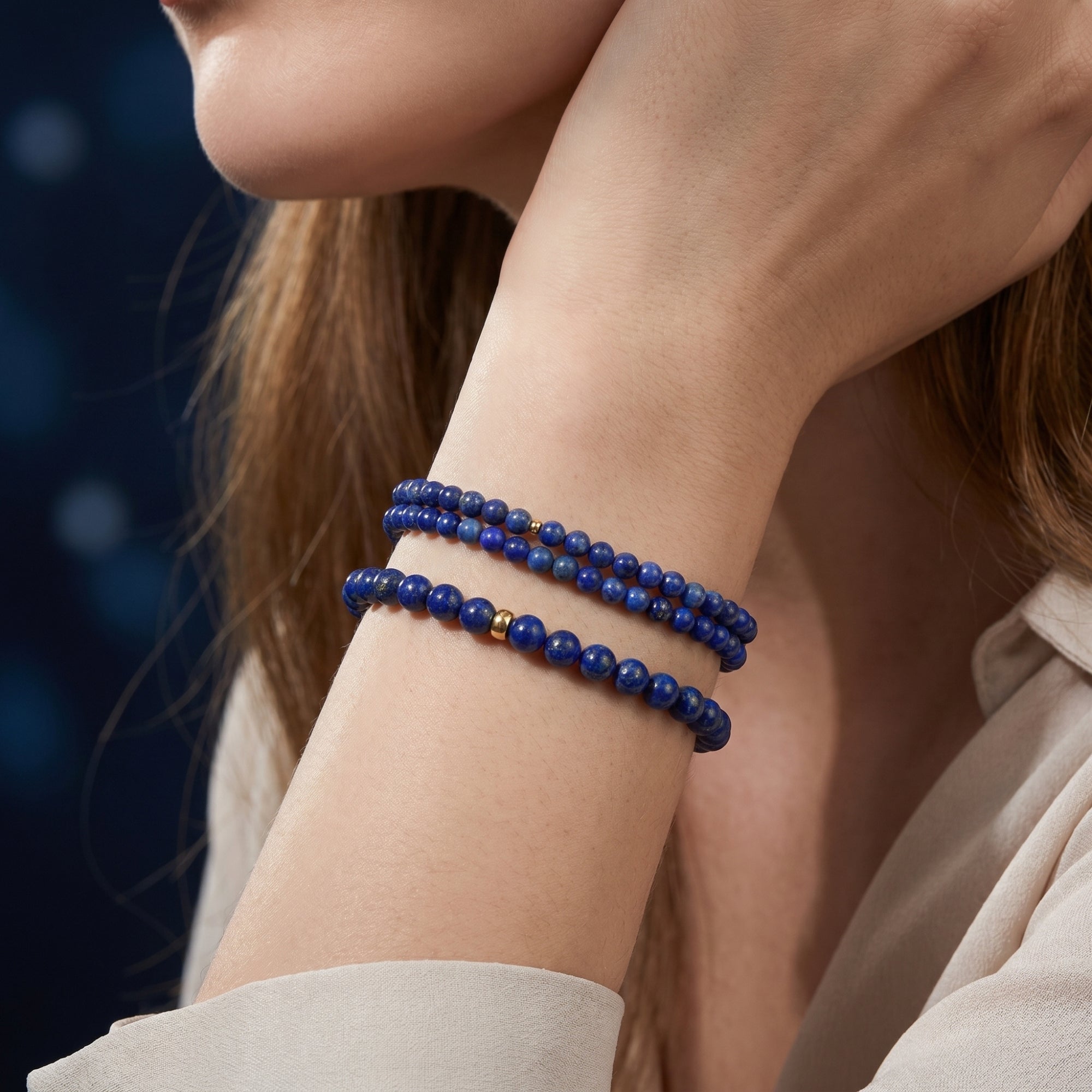 Stacked 4mm and 6mm natural lapis lazuli beaded bracelets with gold spacers worn on a woman's wrist.