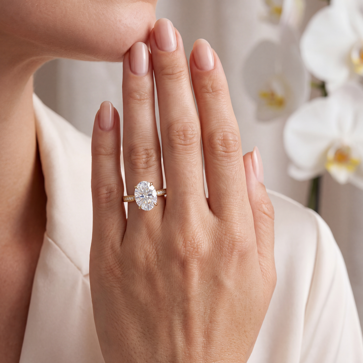 A woman's hand displaying an oval moissanite ring on a yellow gold band with milgrain detailing.