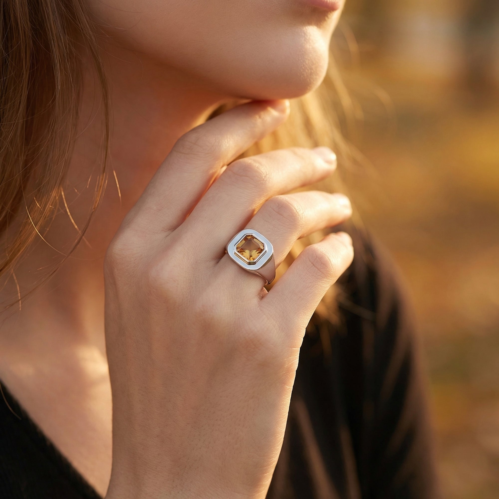Model wearing the silver Asscher-cut natural citrine ring on her finger against a warm outdoor background.