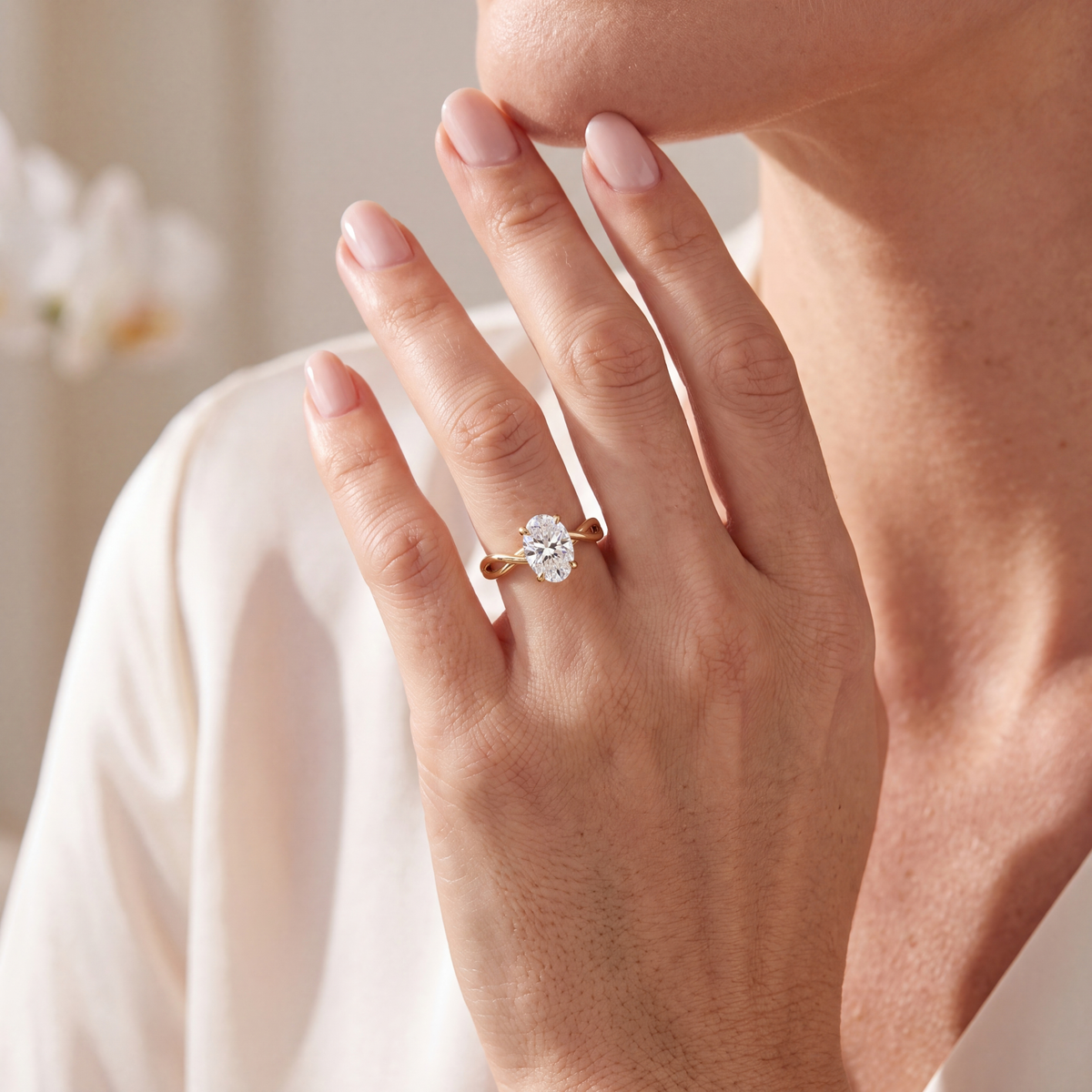 A woman's hand displaying a yellow gold oval moissanite engagement ring with a twisted band.