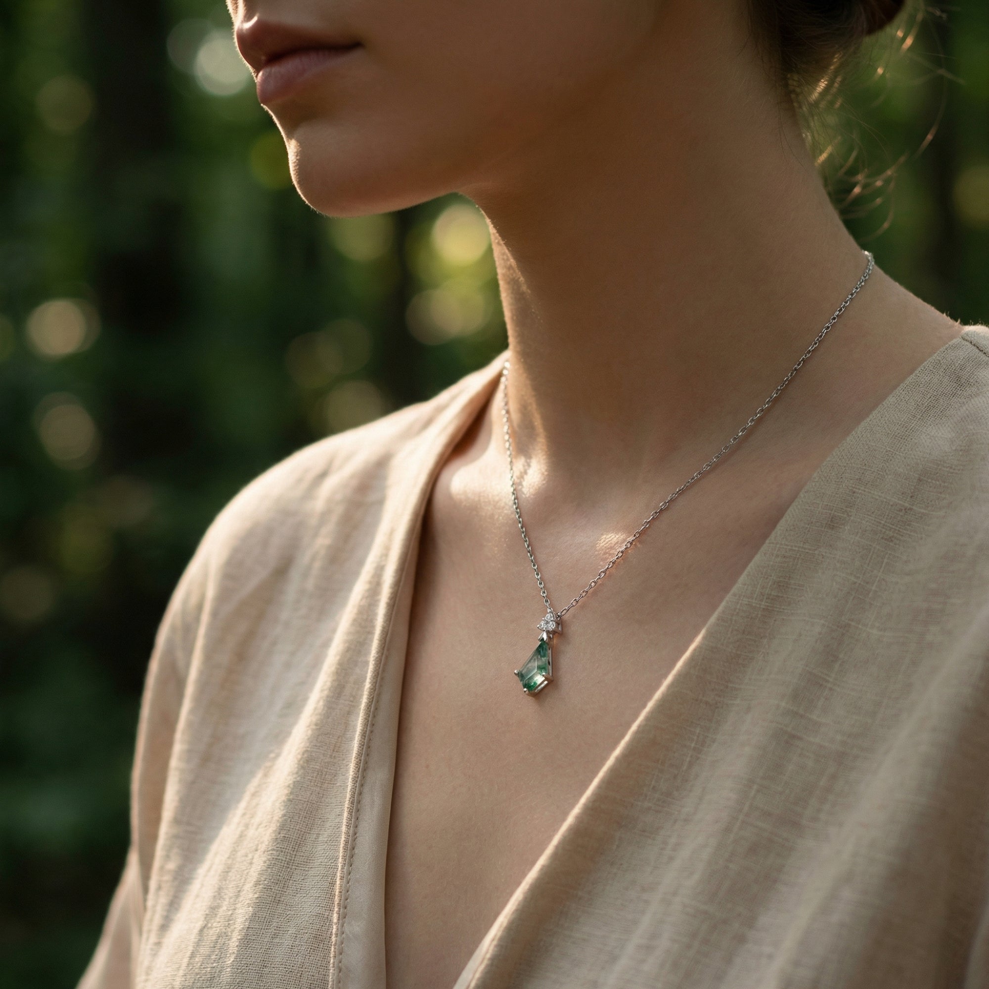 Model wearing a kite cut natural moss agate necklace in sterling silver against a soft outdoor background.