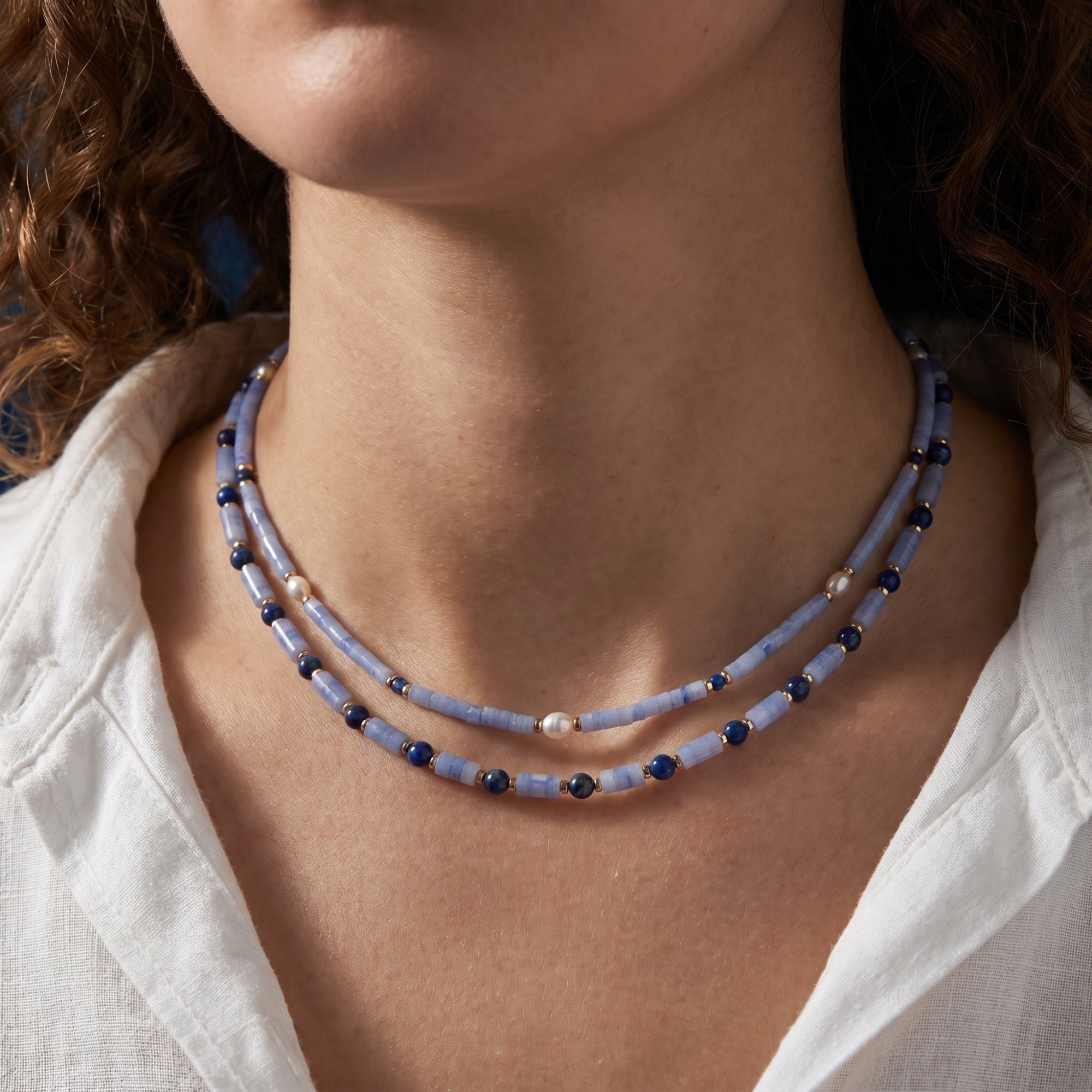 Model wearing the layered gold plated necklace with cylindrical light blue beads, lapis lazuli, and pearls.