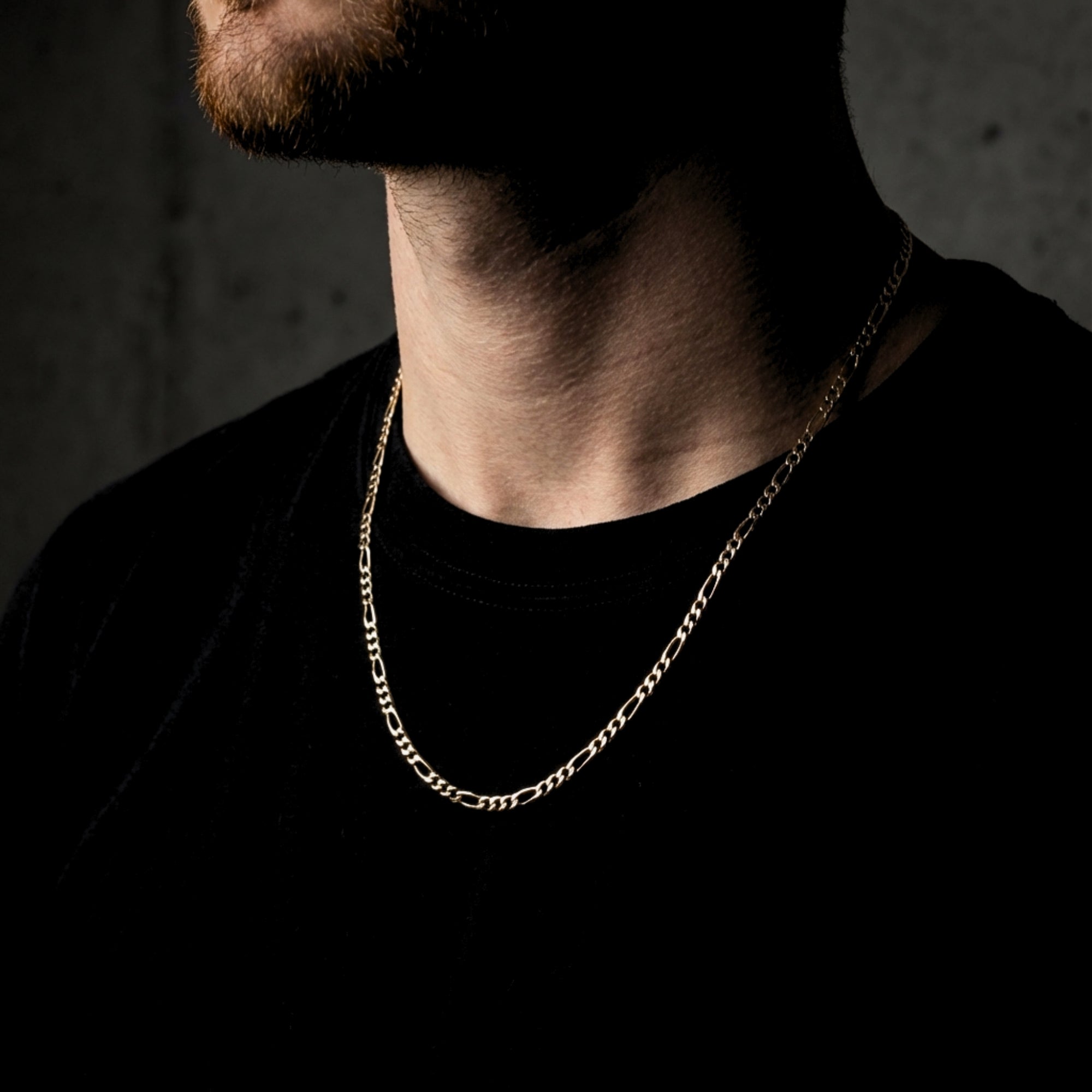 Men's 3mm gold Figaro chain worn by a model over a black t-shirt for a minimalist look.