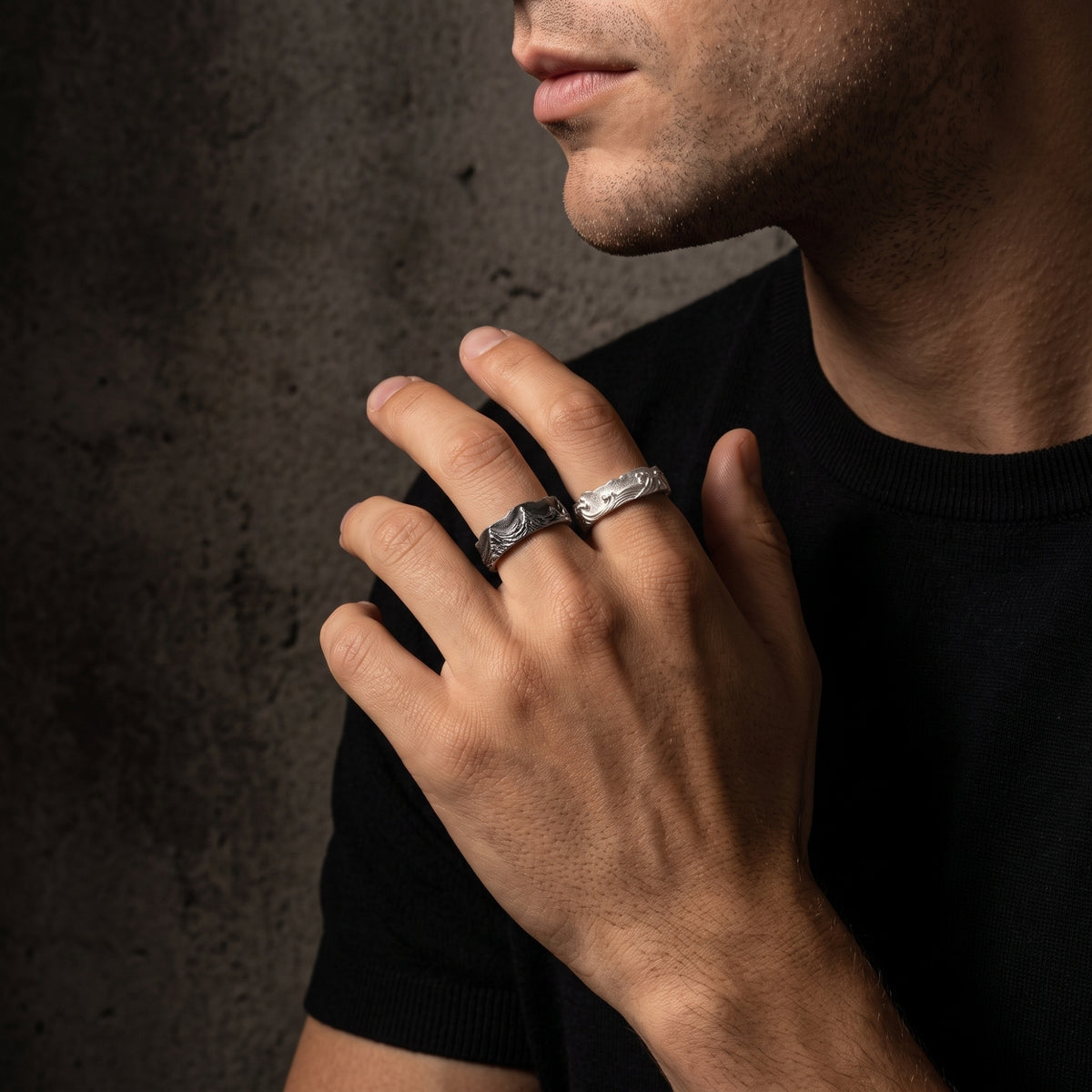 Person wearing dark-toned and bright silver wave open-band rings on adjacent fingers near the face.