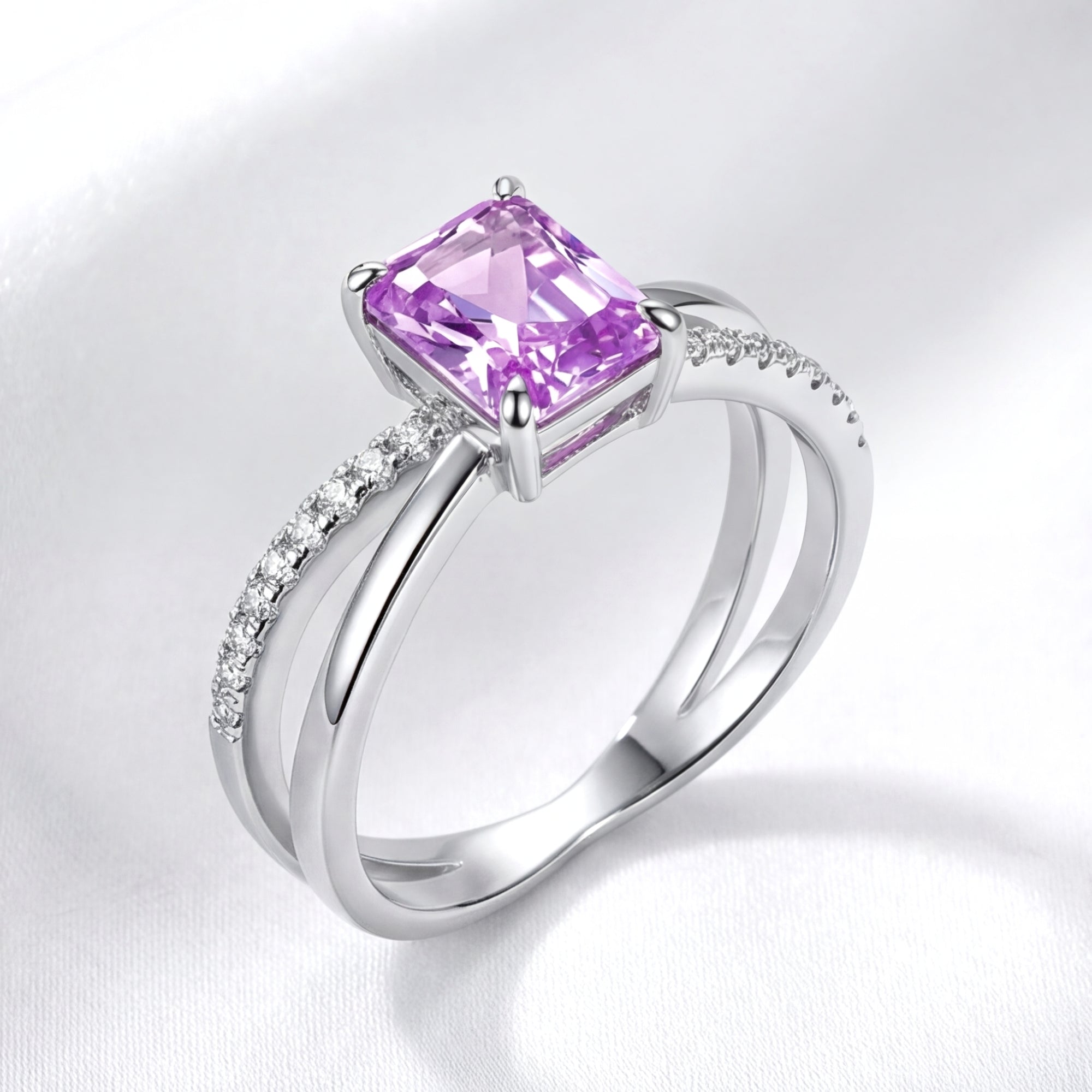 Side profile of the sterling silver Evanthe ring showing the bypass setting and emerald-cut amethyst on white fabric.
