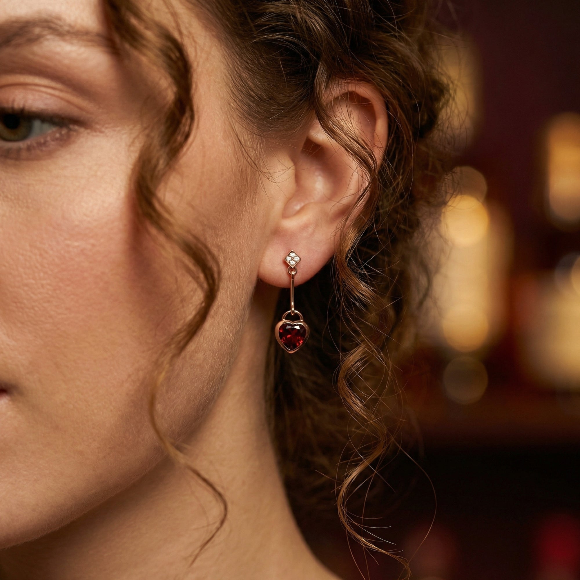 Close-up of a woman wearing a Rosalette 18K rose gold drop earring featuring a heart-cut red garnet gemstone.