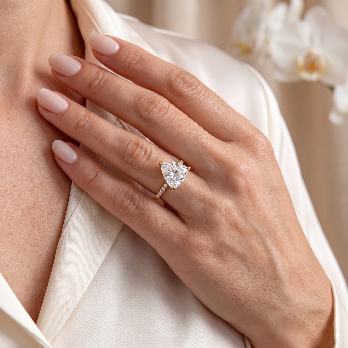 A hand wearing a yellow gold trillion-cut moissanite engagement ring with a pavé band.