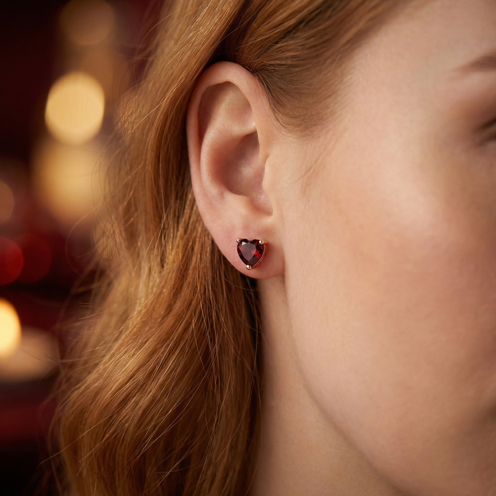 Woman wearing a heart-cut natural garnet stud earring in 18K rose gold on her earlobe.
