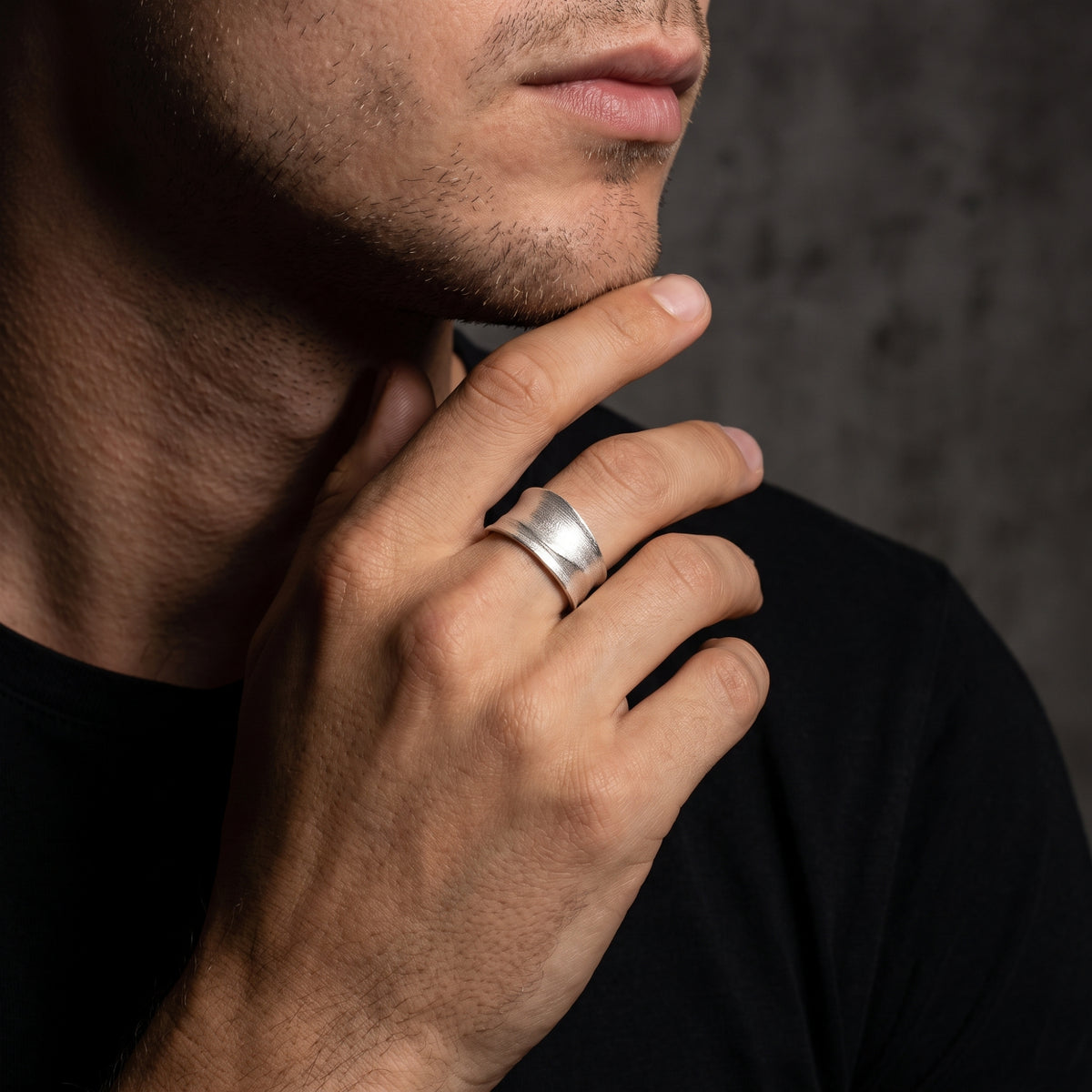 Man wearing a wide brushed silver contour ring while touching his chin.