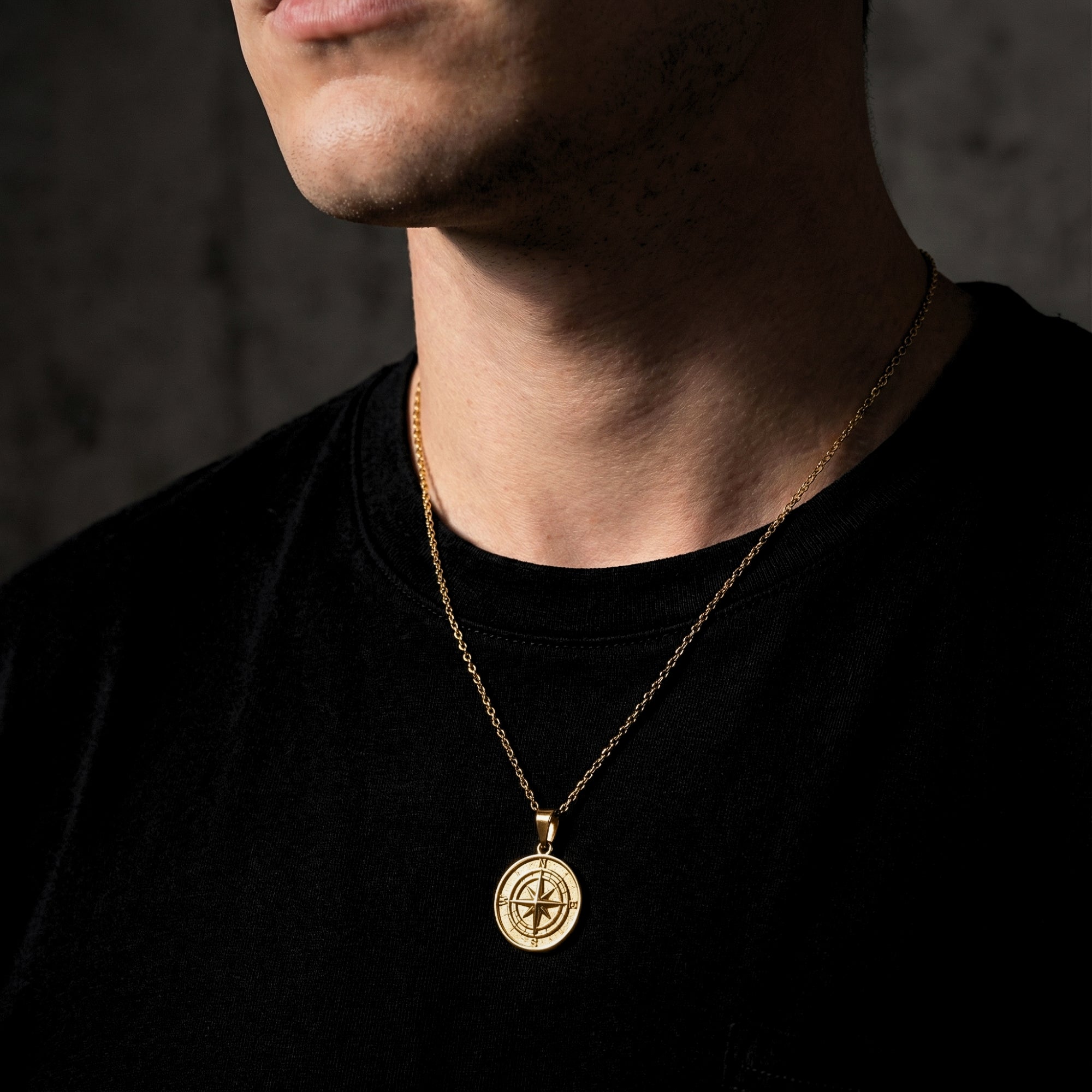Model wearing the gold stainless steel Voyager compass pendant necklace over a black t-shirt.