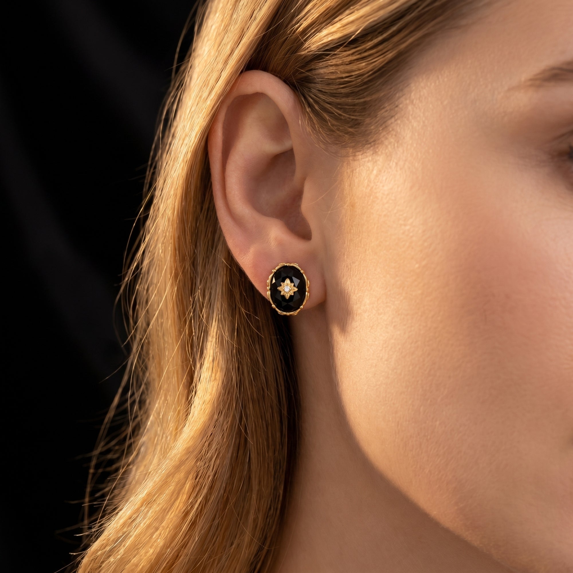 Model wearing a yellow gold oval-cut faceted black onyx earring with a gold starburst center.