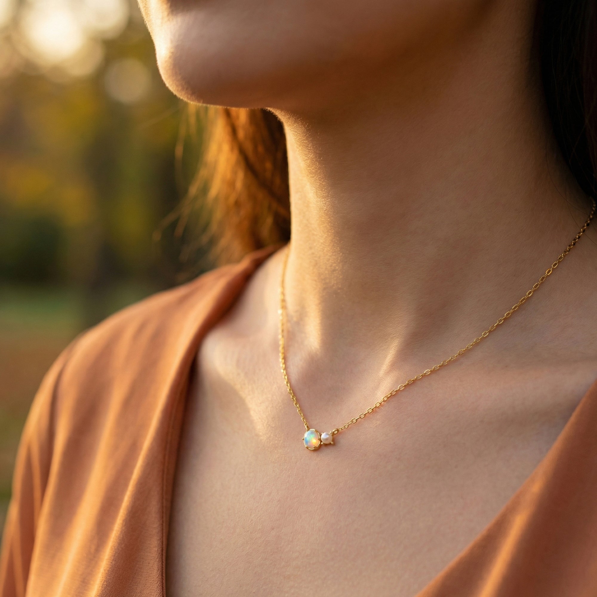 Minimalist gold oval white opal and pearl necklace worn by a model in natural outdoor light.