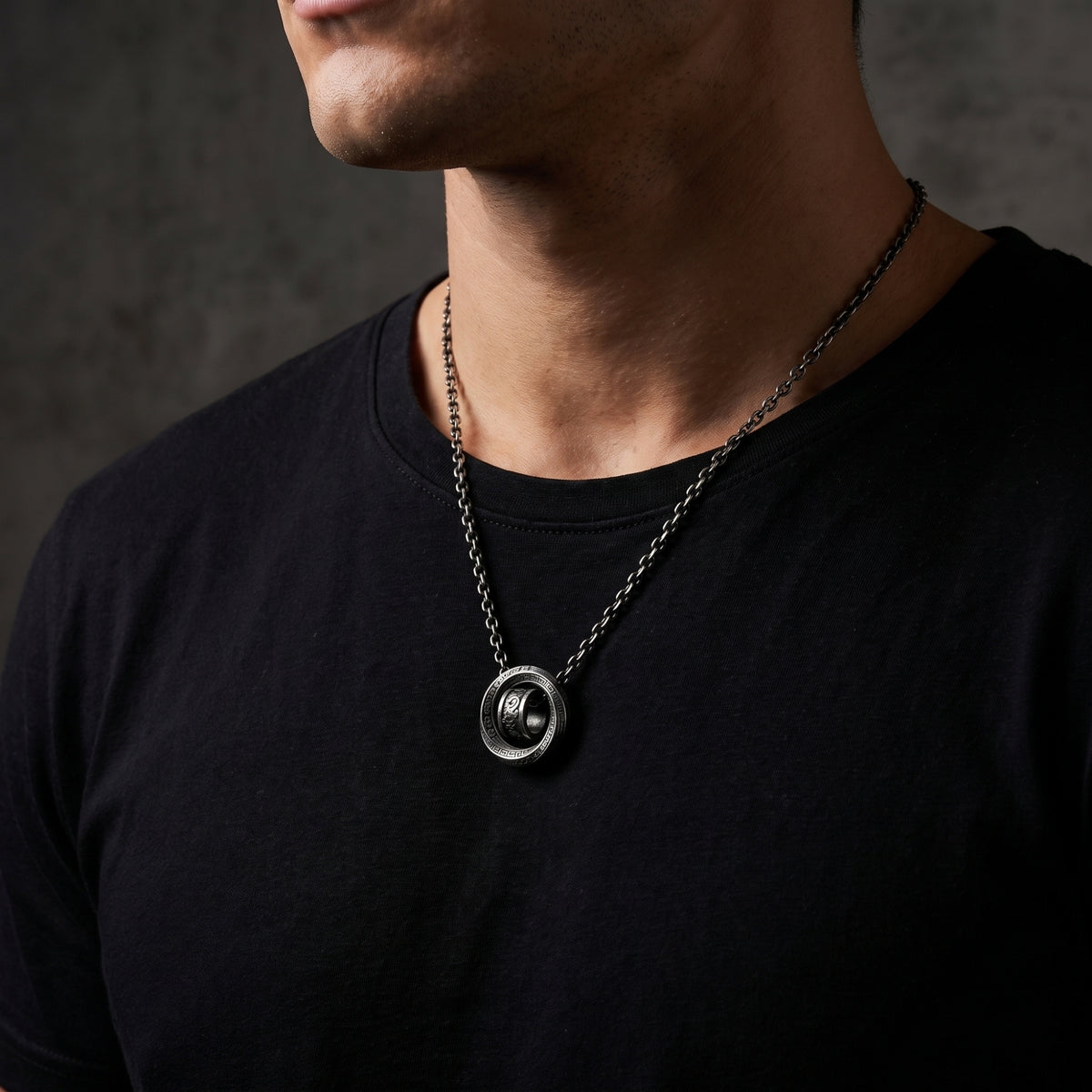 Three-quarter close-up of a man wearing the double-ring pendant necklace over a black T-shirt.