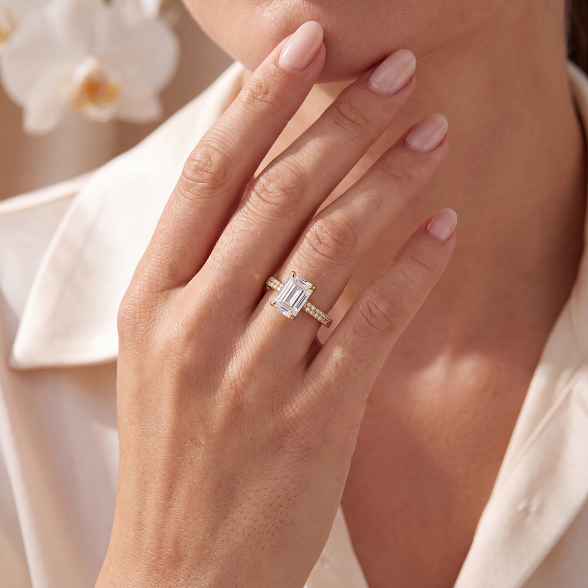 Model wearing a gold emerald-cut moissanite engagement ring with double-row pavé band.
