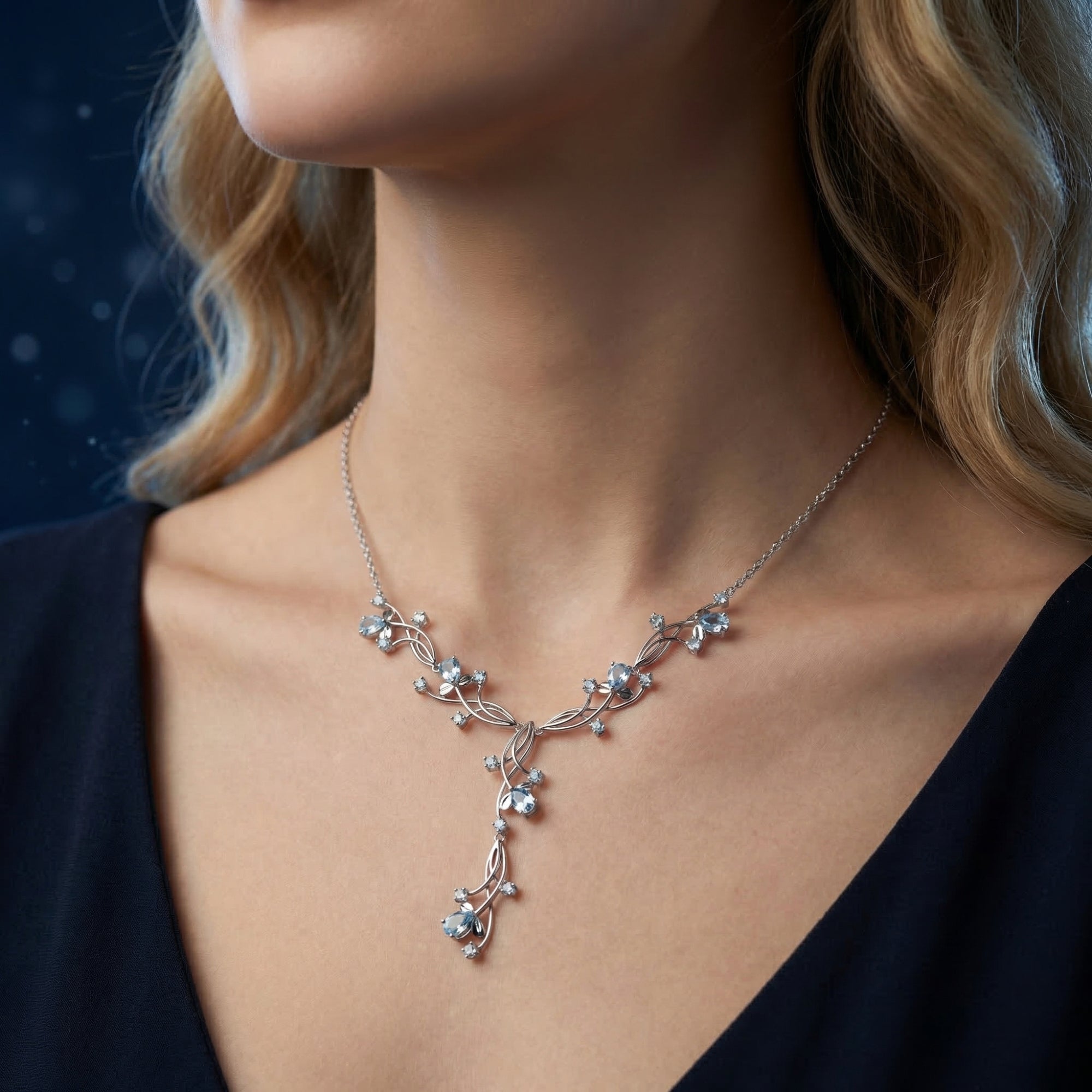 Model wearing the Loredana natural blue topaz necklace in white gold, showing the elegant vine-like pendant.