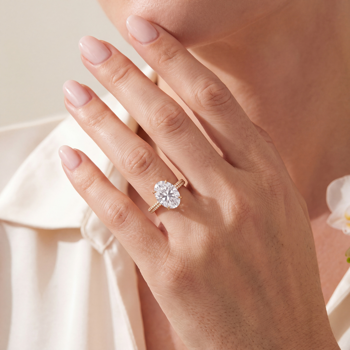 Model wearing an oval moissanite yellow gold engagement ring on her hand resting near her chin.