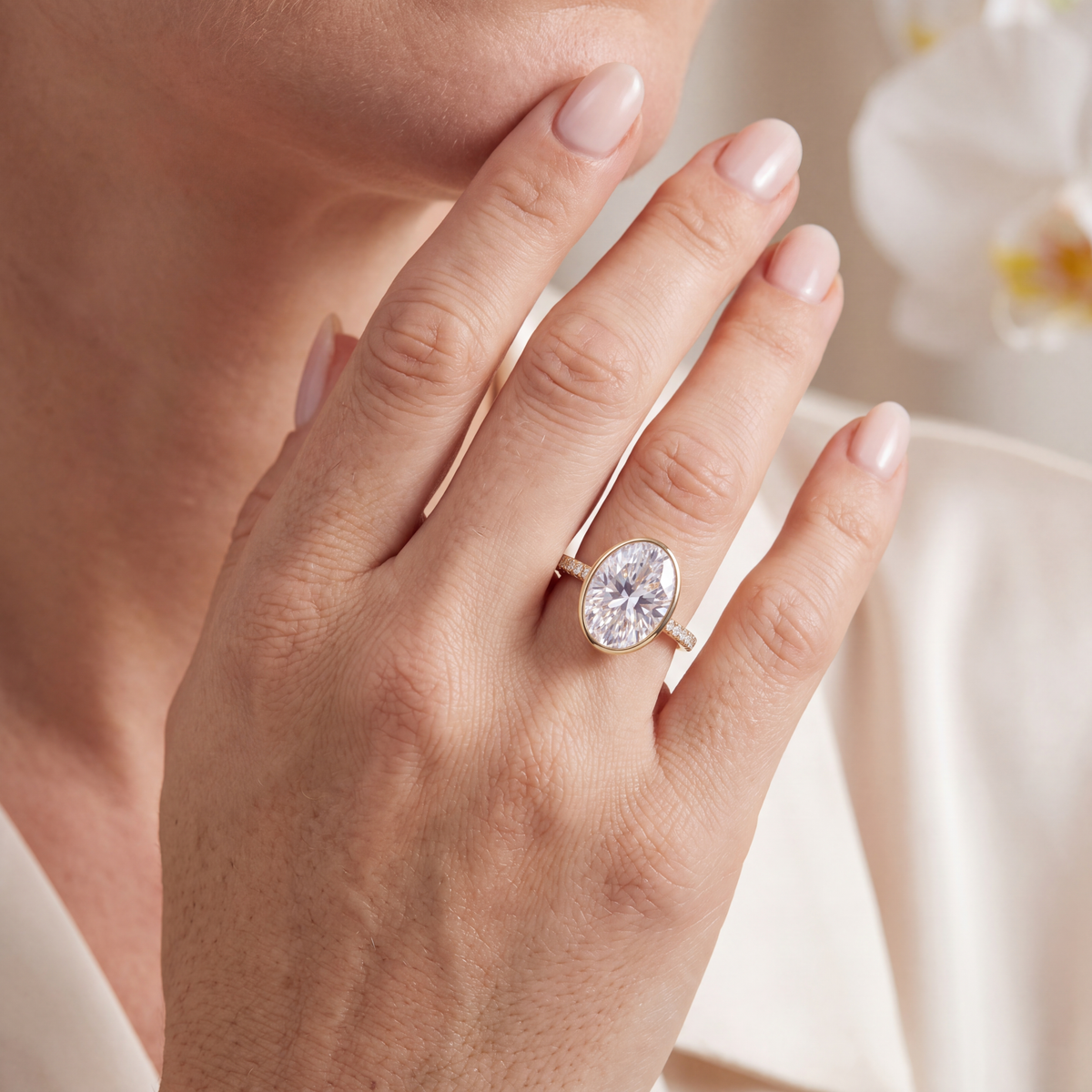 Model wearing an oval moissanite bezel engagement ring with a pavé yellow gold band.