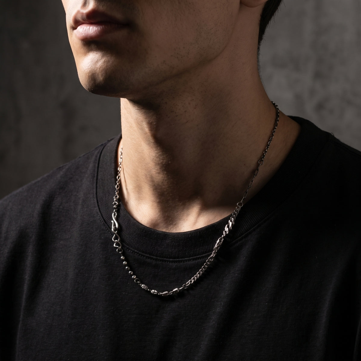 Silver multi-link necklace worn around a model’s neck over a black shirt, shown in a left-facing profile.