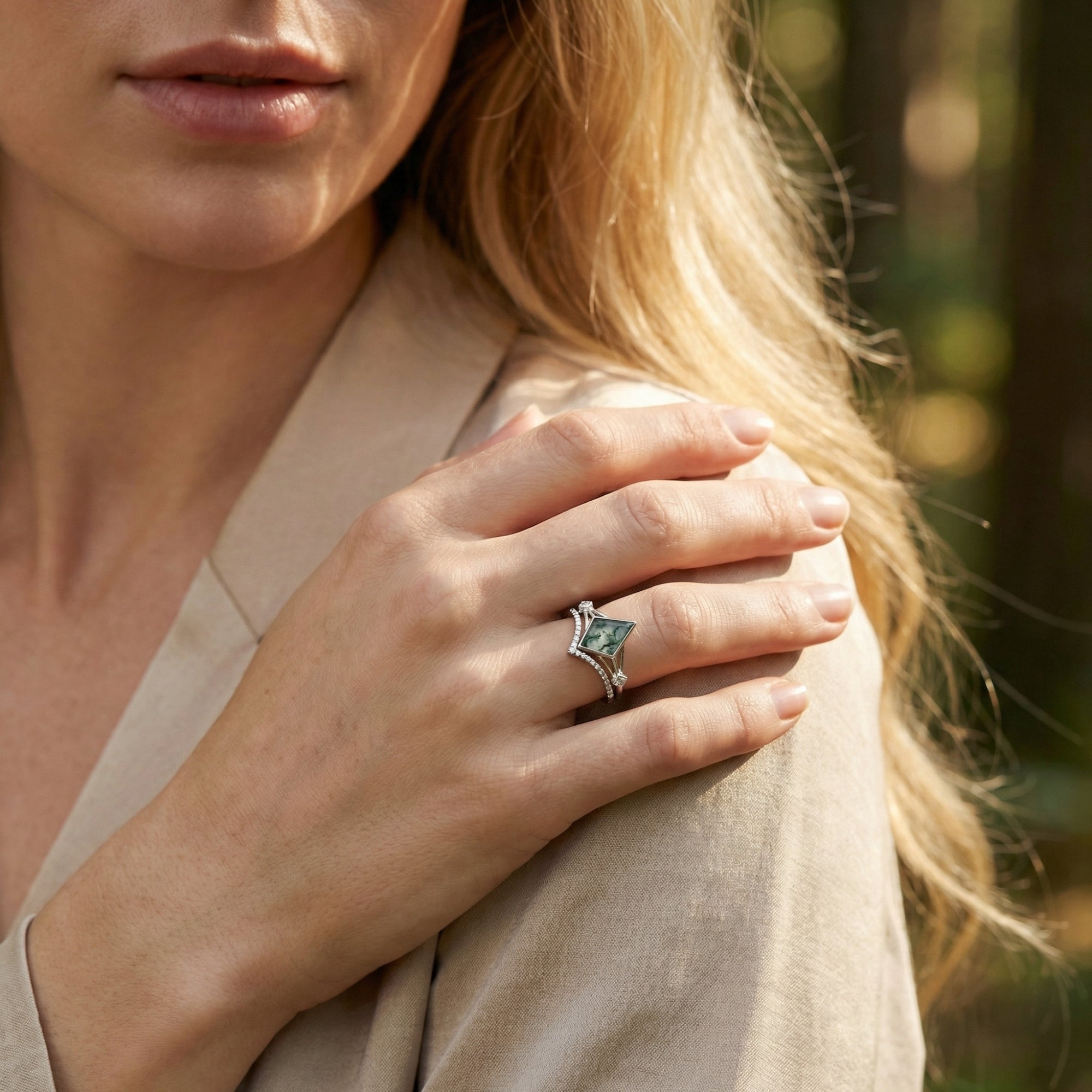 Model wearing a kite cut moss agate S925 sterling silver ring set on her finger against a soft outdoor background.