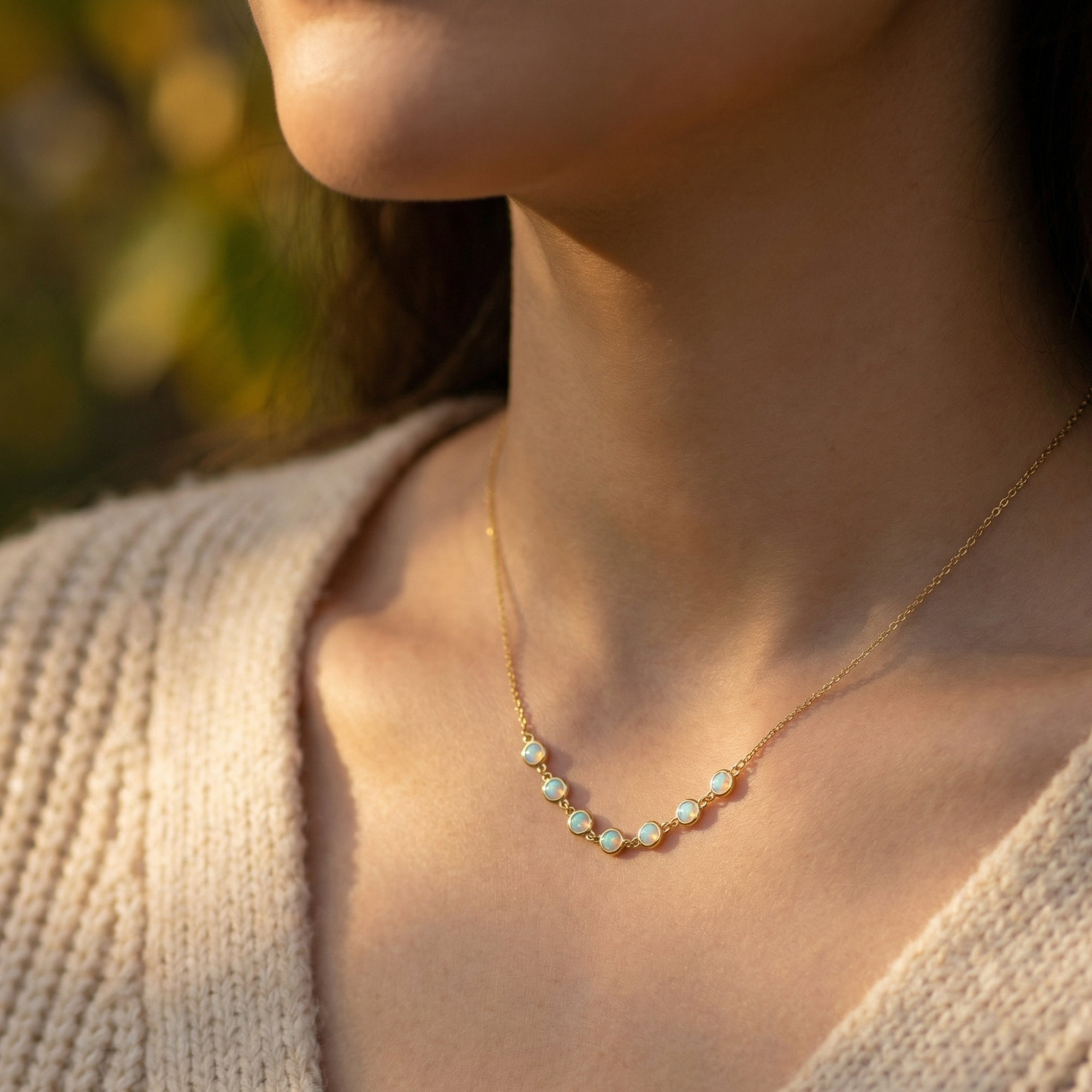 Gold-tone Lumina necklace with seven round white opals worn by a woman in warm outdoor light.