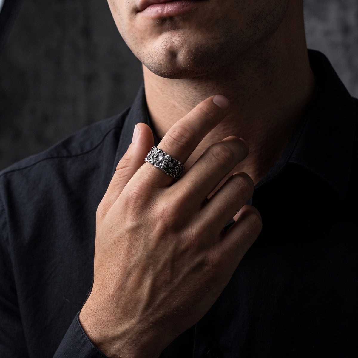 Model wearing the wide carved silver fleur-de-lis ring on his index finger near his jaw.