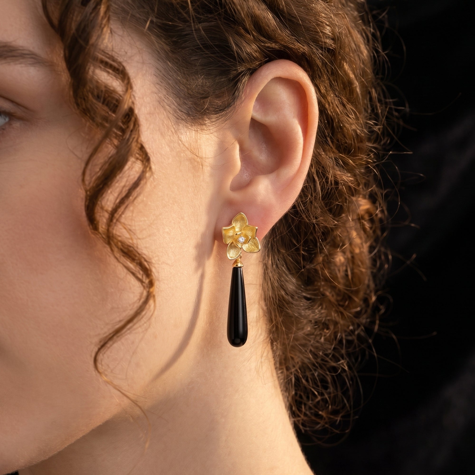 18K gold plated Calla floral drop earring with an elongated black onyx stone worn on a model's ear.