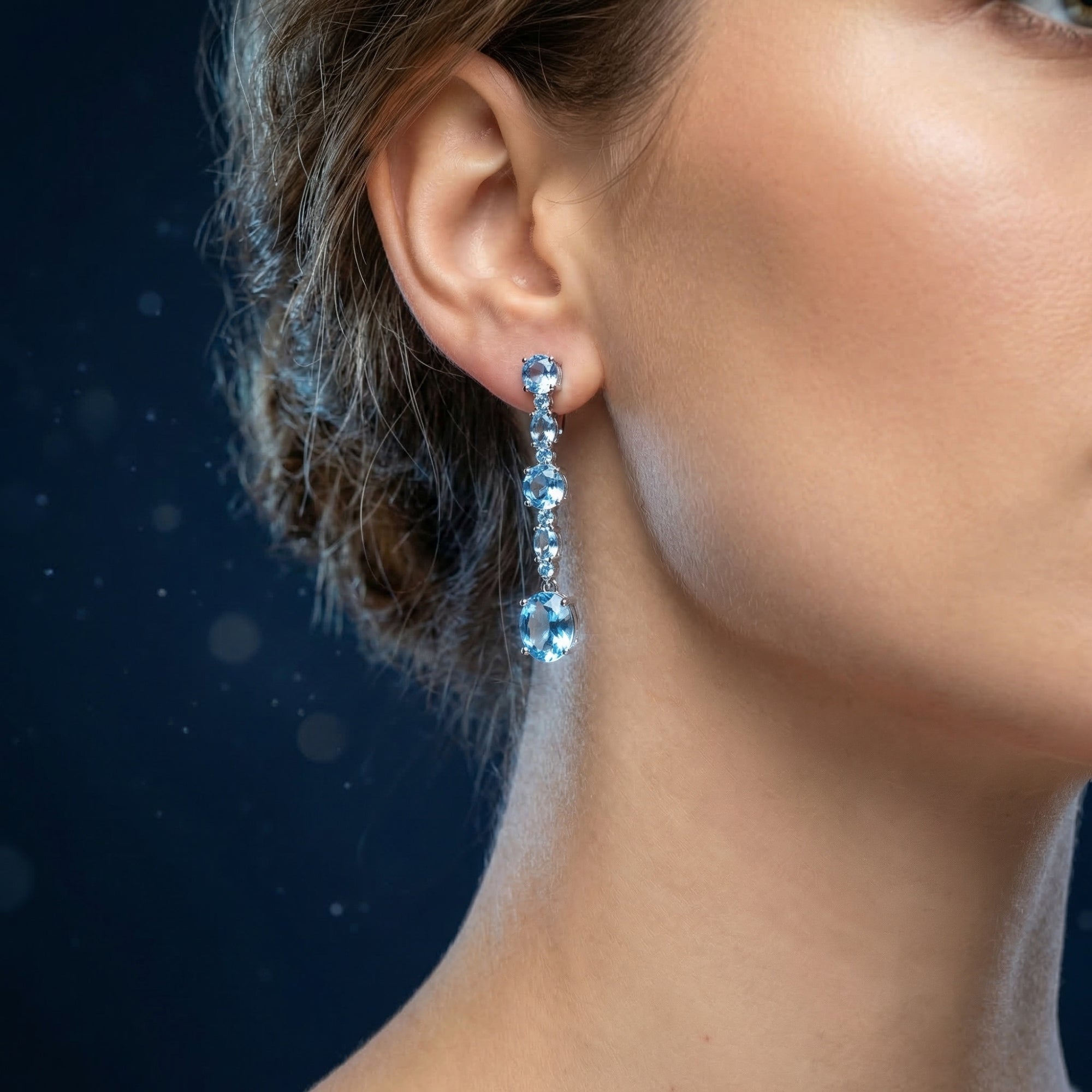 Close-up of a woman wearing a silver drop earring with a cascade of round and oval natural blue topaz stones.