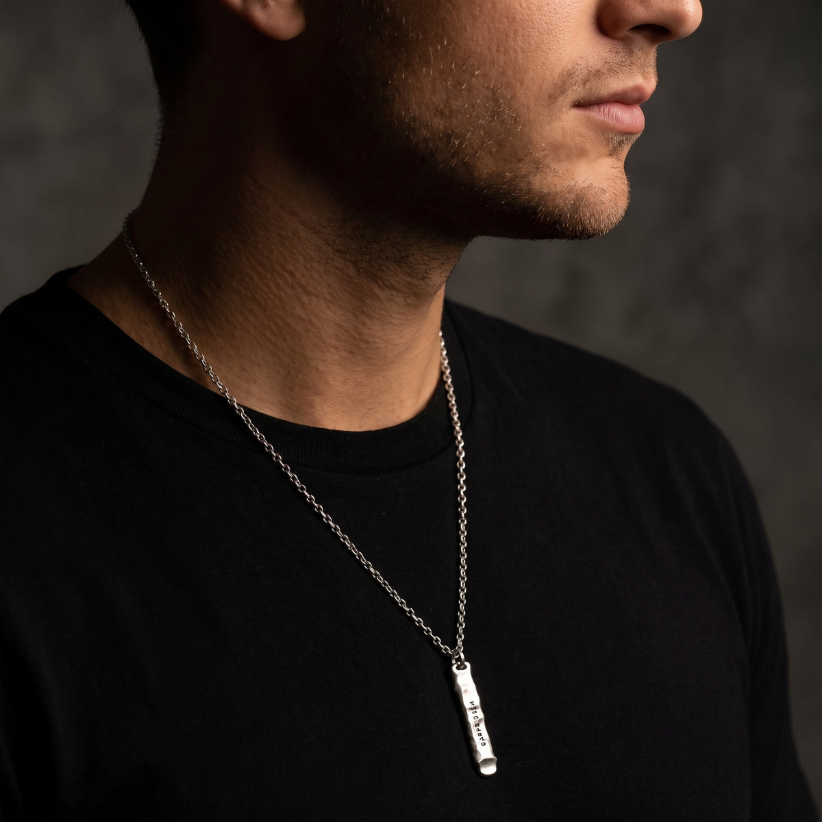 Man wearing the silver bar pendant necklace over a black crewneck shirt.