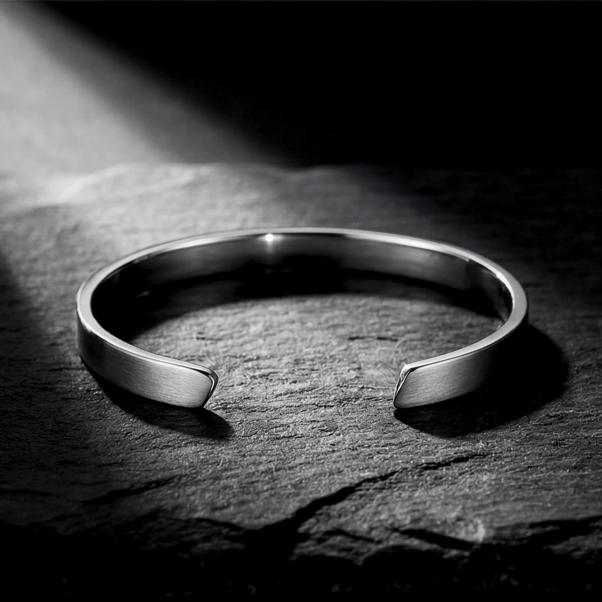 Open silver stainless steel cuff bracelet with a brushed finish on a dark stone background.