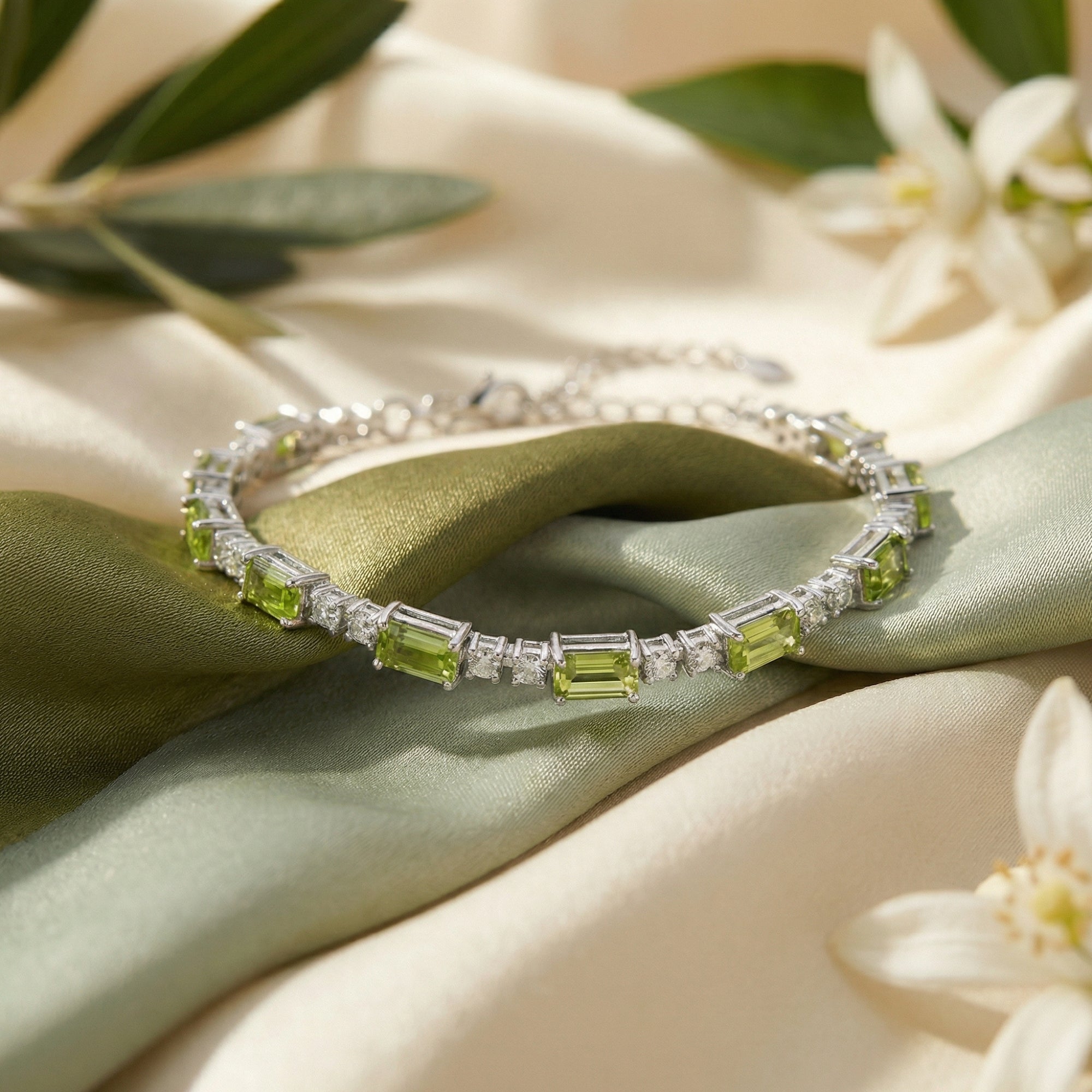 Sterling silver tennis bracelet with emerald cut peridot stones on draped green silk and olive branches.