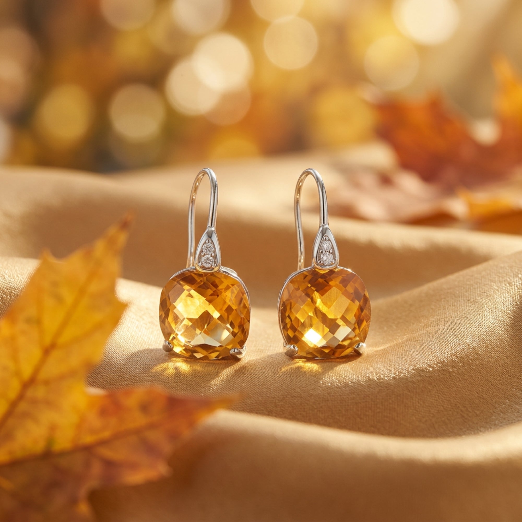 Pair of silver cushion-cut natural citrine drop earrings displayed on draped fabric with fall leaves.