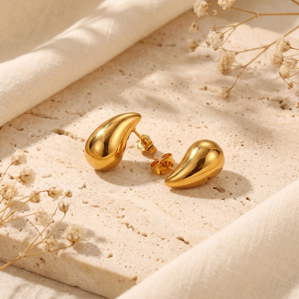 Paire de boucles d’oreilles en goutte dorées et polies sur pierre beige, avec tiges et fermoirs papillon visibles.