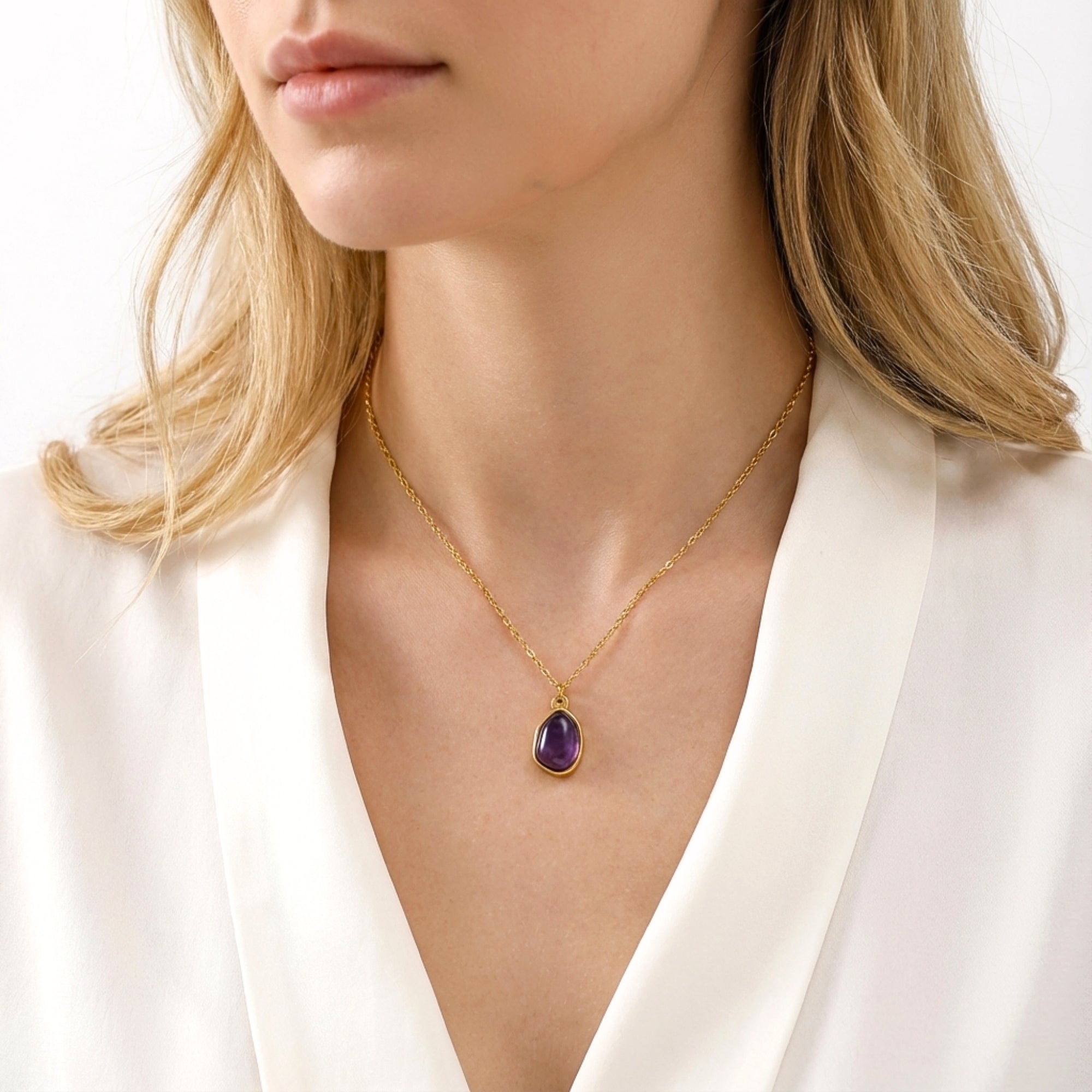 The Isadora teardrop simulated amethyst necklace in yellow gold worn by a model with a white blouse.