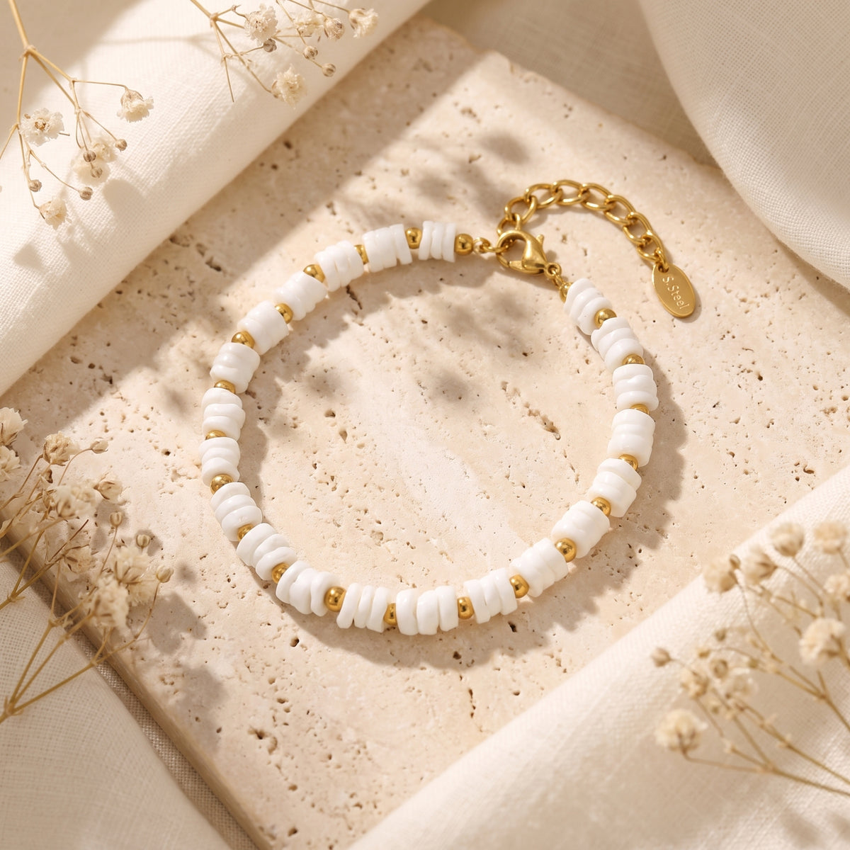 White disc-bead bracelet arranged on a beige stone slab, with its clasp, extension chain, and tag visible.