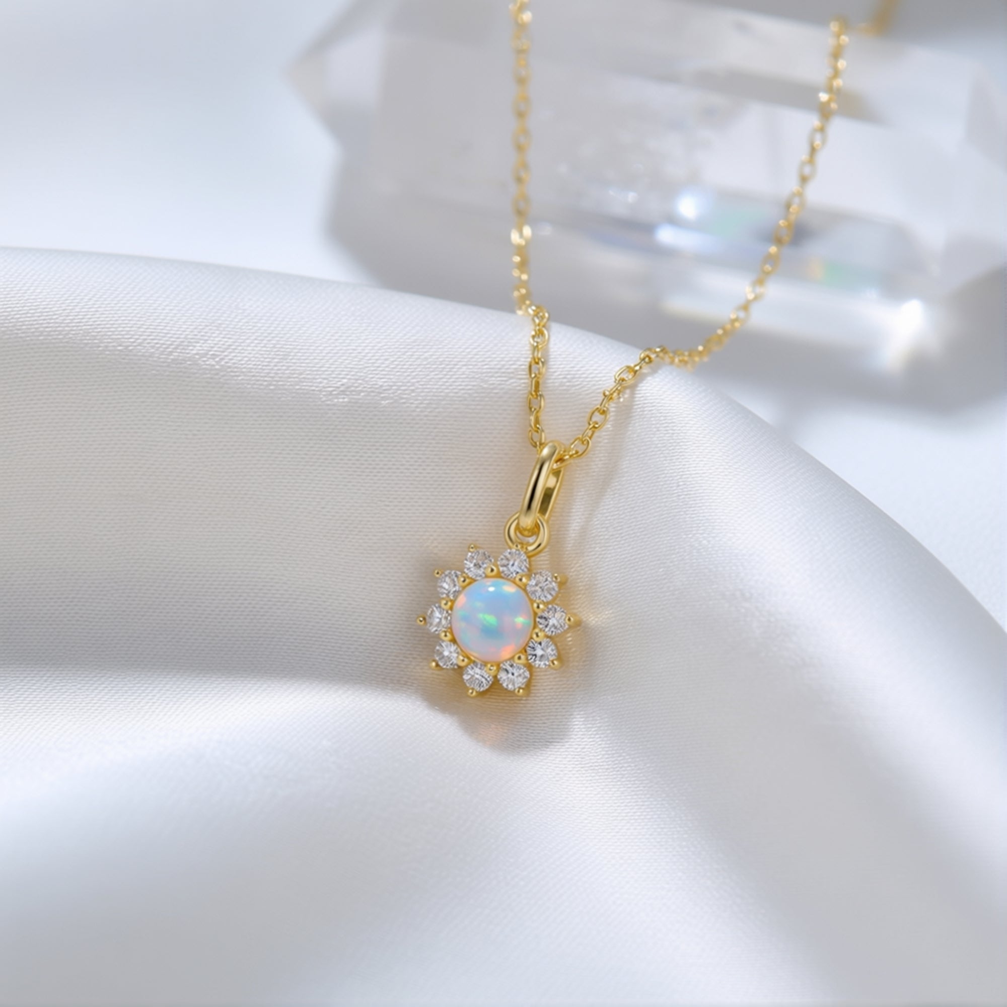 Close-up of the Celestria round white opal pendant with a sparkling halo in a gold-tone setting on white silk.