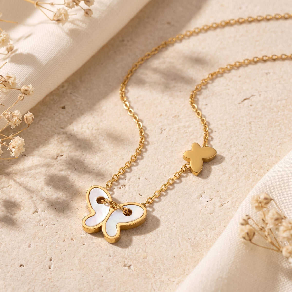 Angled close-up of a gold-tone butterfly station necklace with mother-of-pearl pendant and small butterfly charm