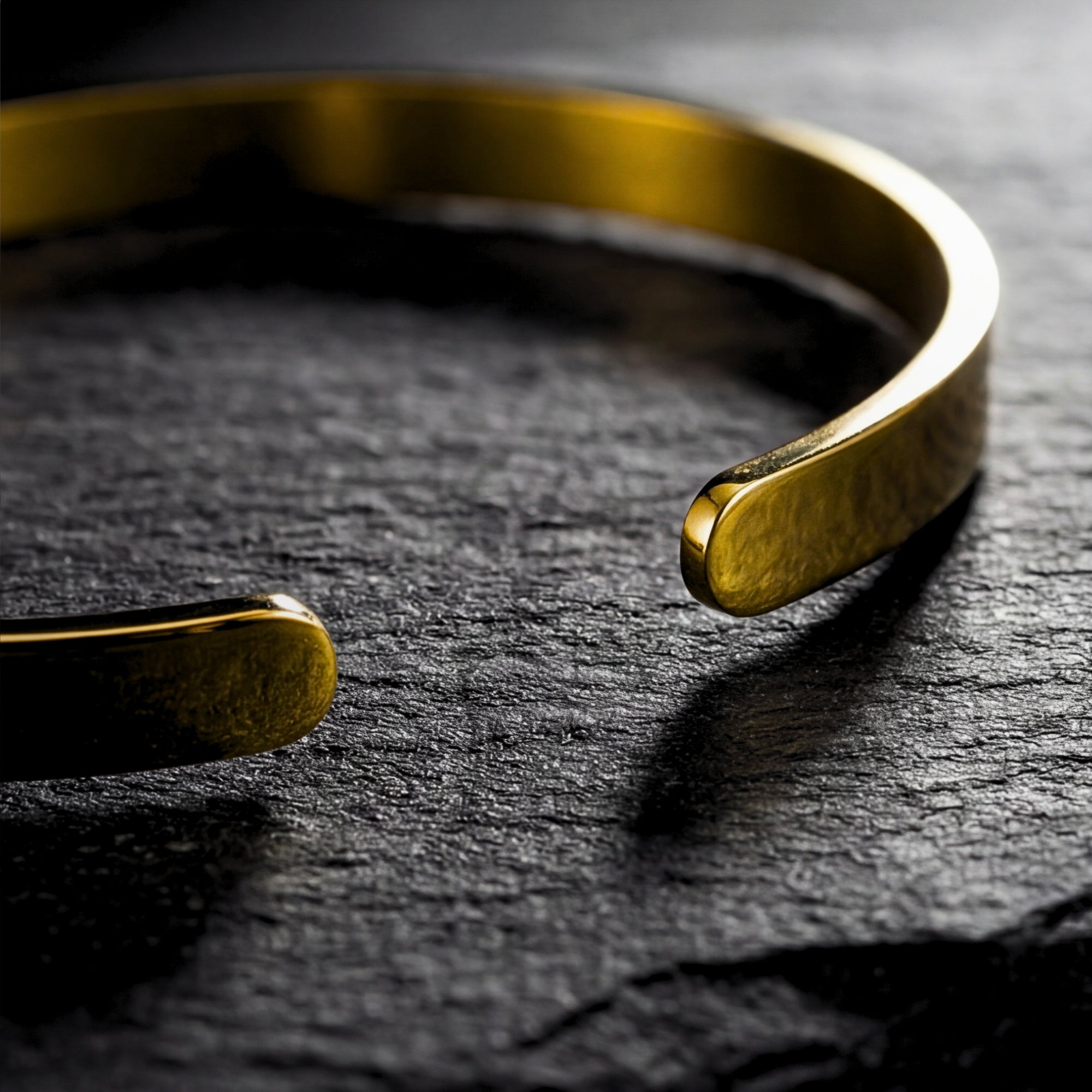 Macro view of the rounded ends and polished gold finish of a men's stainless steel cuff bracelet.