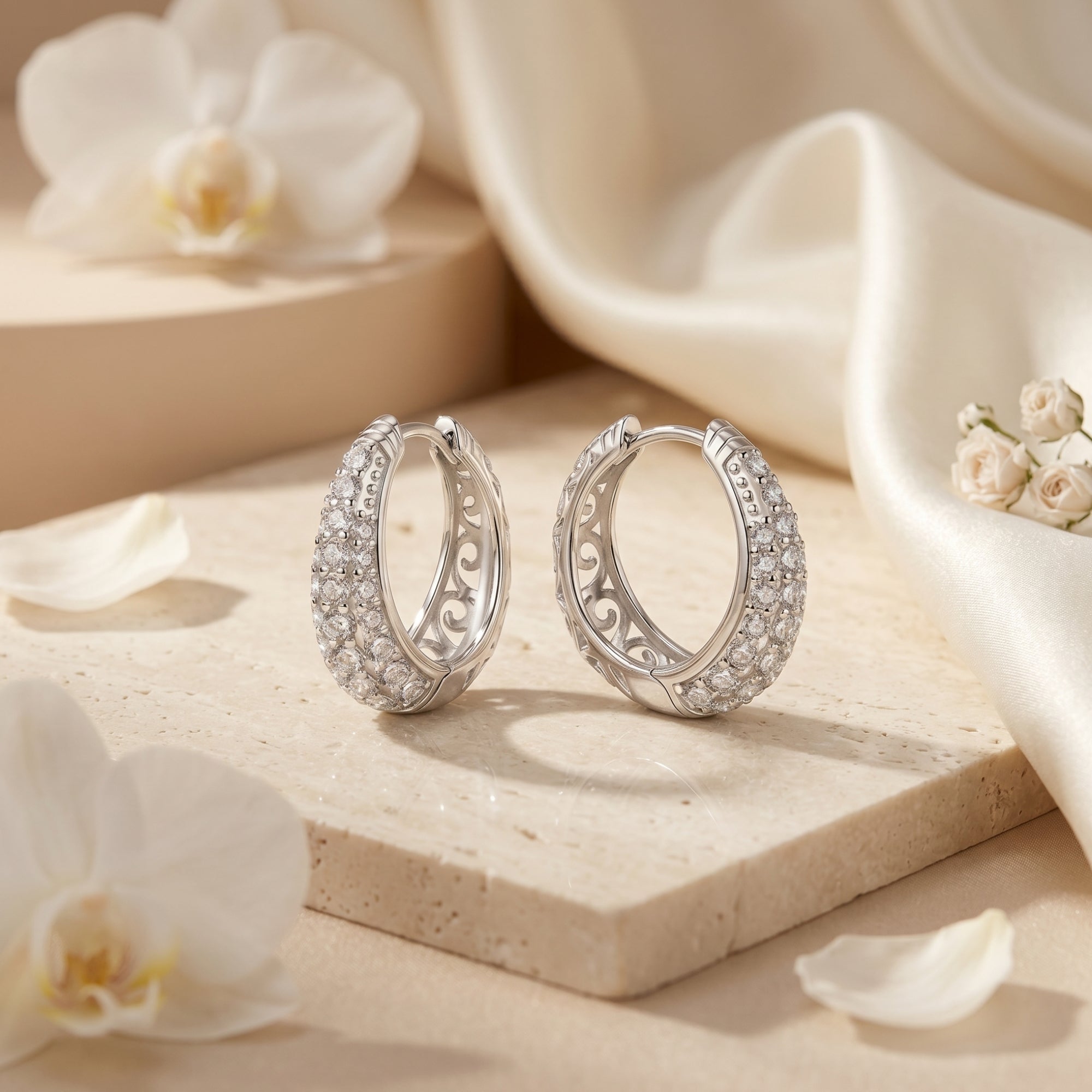 Silver round-cut moissanite hoop earrings on a stone surface with white flowers and silk.