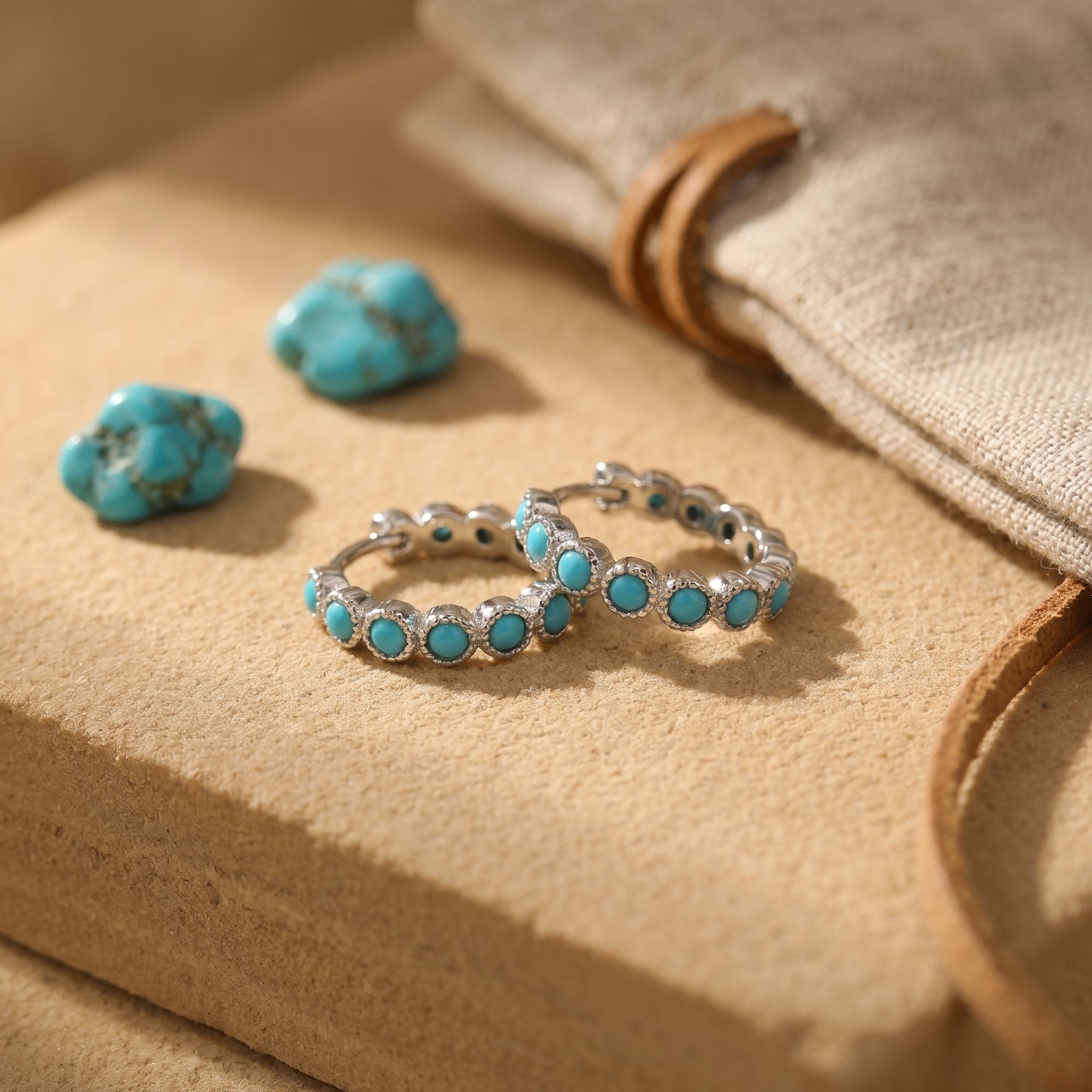 Sterling silver huggie earrings featuring round turquoise cabochons on a textured desert-inspired surface.