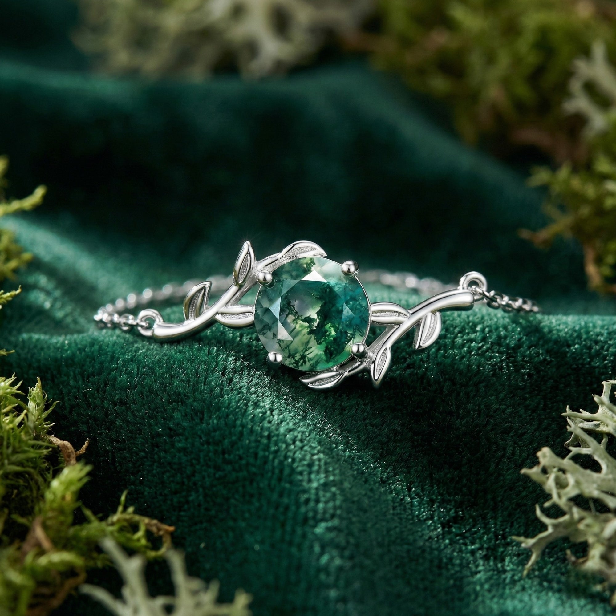 Close-up of the round moss agate stone and intricate sterling silver vine leaf setting on a green velvet surface.