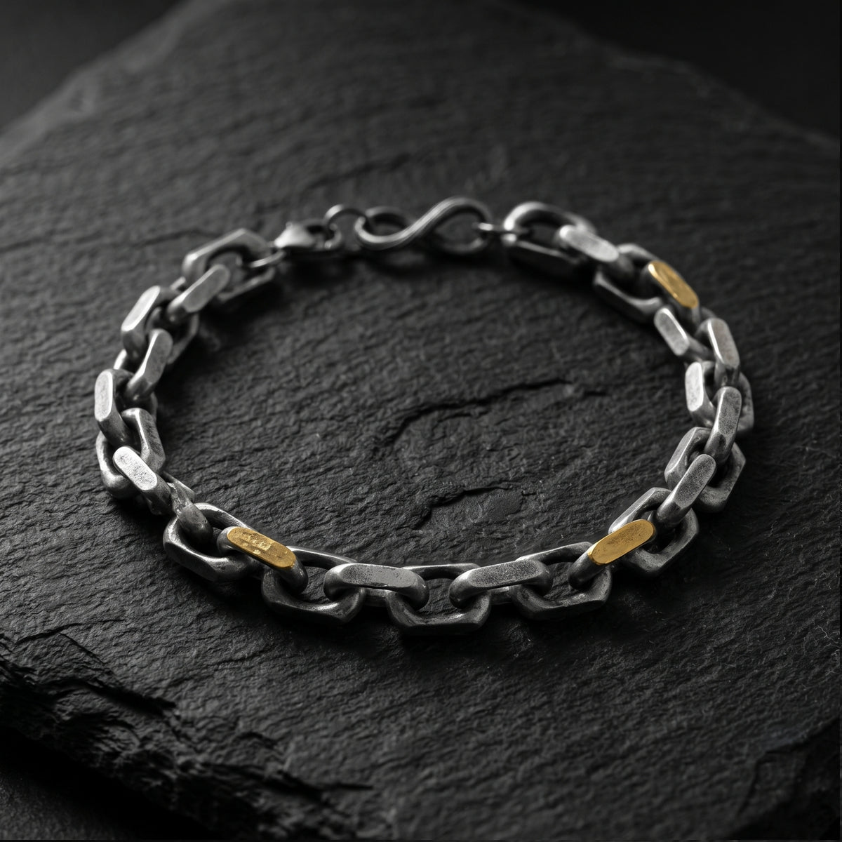 Full-length overhead view of the silver and gold-tone link chain bracelet arranged on dark slate.
